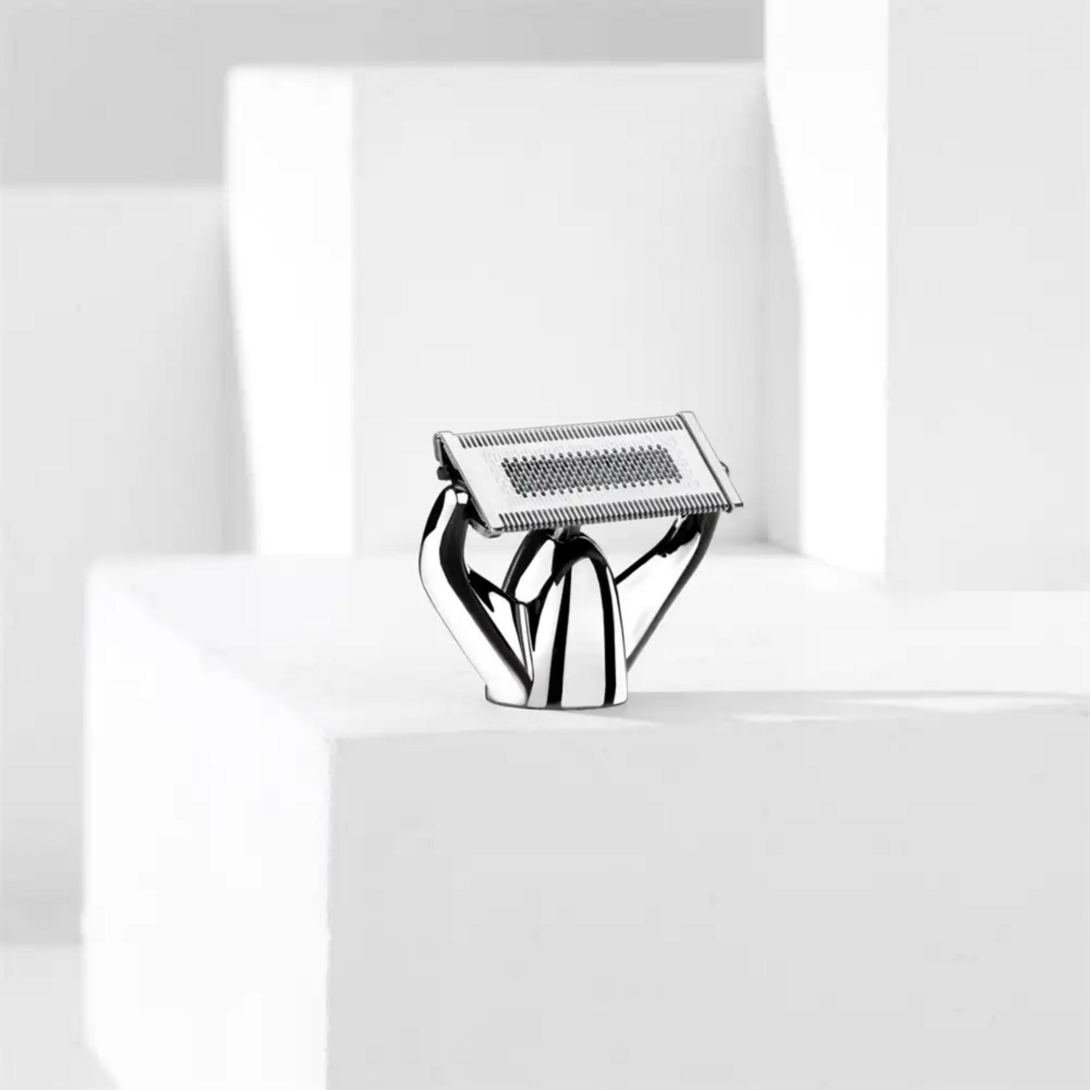 Srebrna maszynka do golenia na białym postumencie, ze światłem i cieniem.