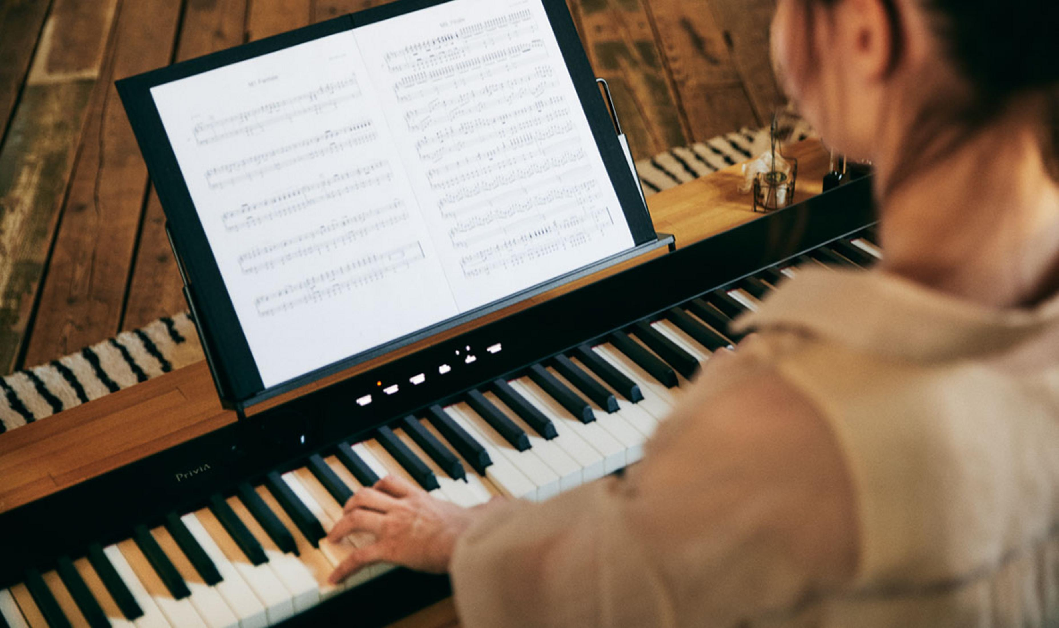 Een persoon bespeelt een digitale piano met bladmuziek op een standaard.