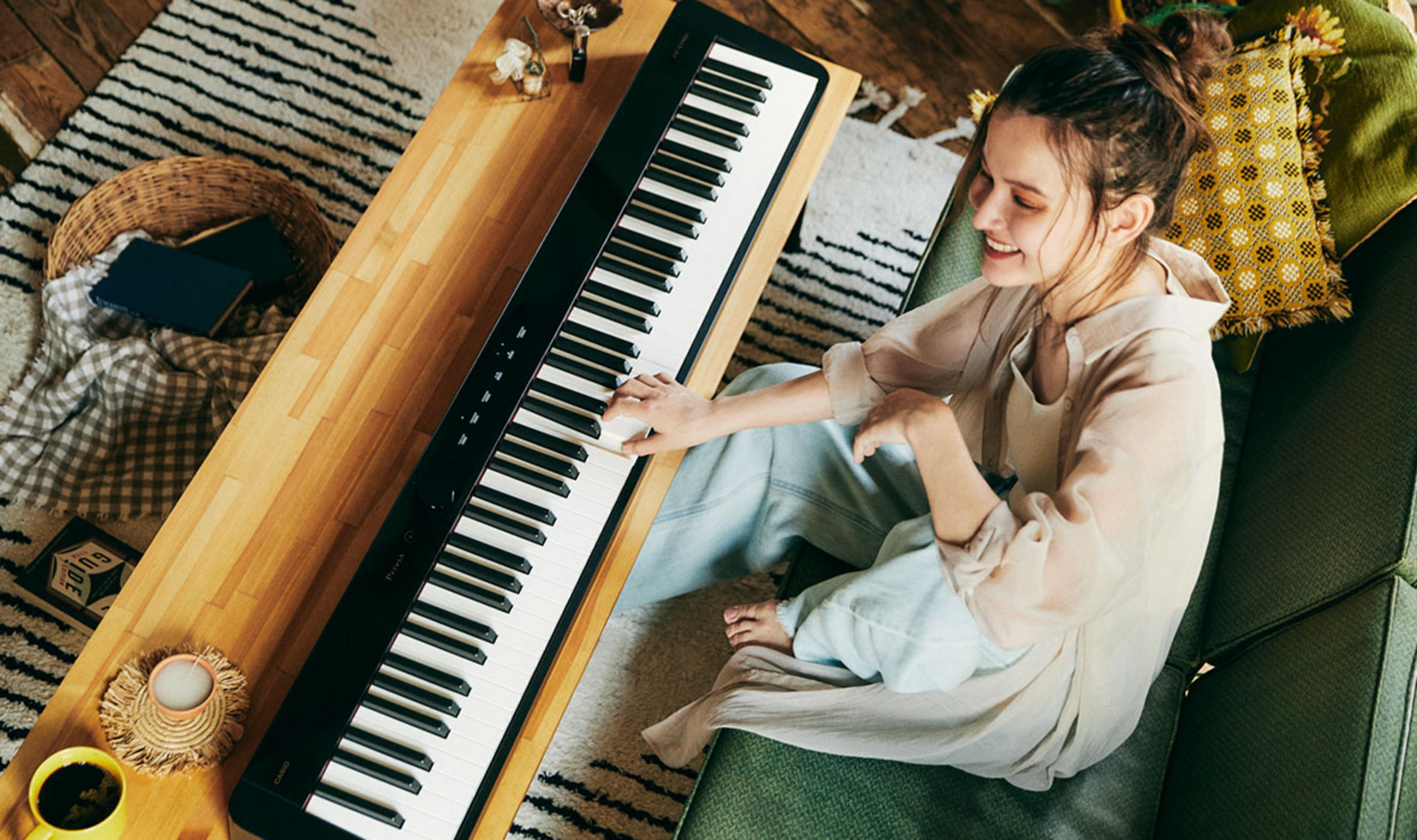 Een vrouw speelt op een zwart digitaal piano in een knusse kamer.
