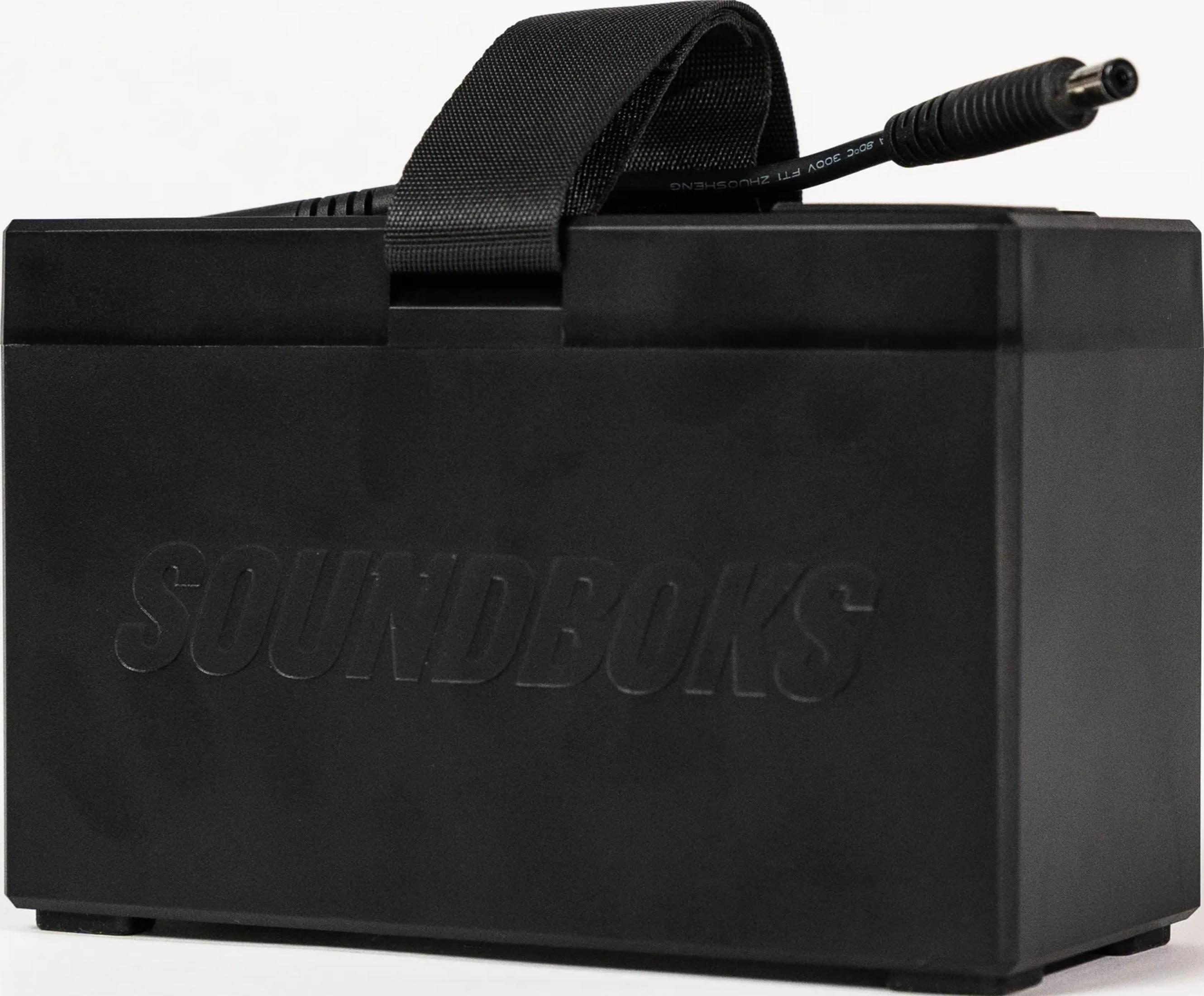 Schwarzer Kasten mit „SOUNDBOKS“ Schriftzug, Tragegriff und Kabel.