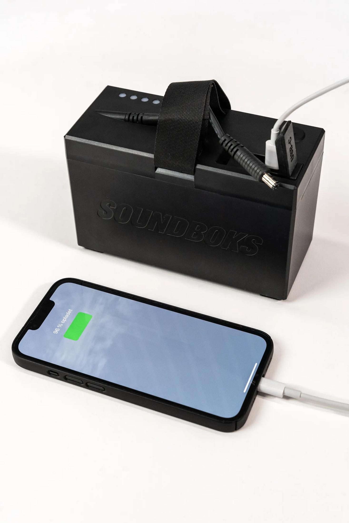 Schwarzer SOUNDBOXS Lautsprecher wird zum Aufladen eines Telefons angeschlossen.