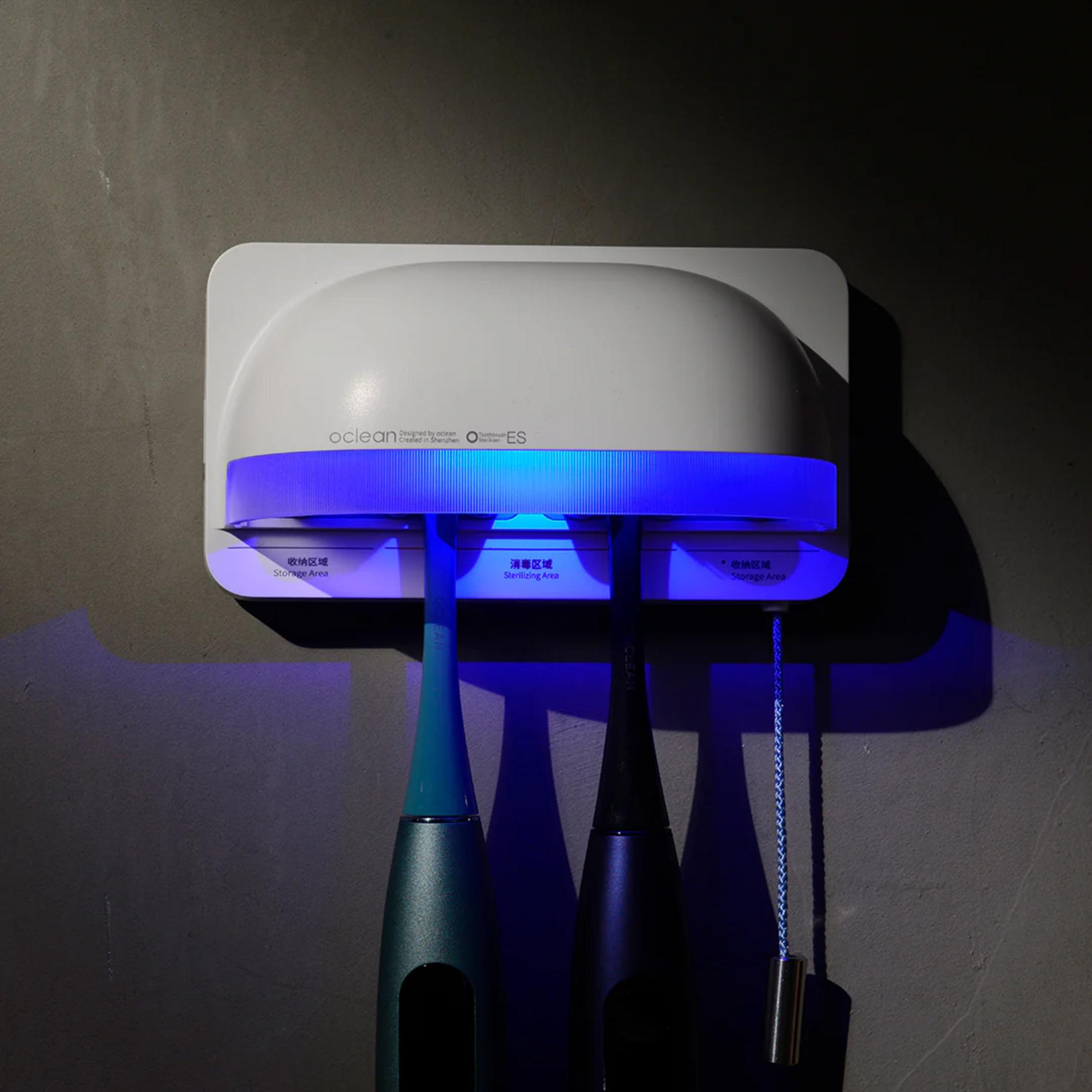 Un esterilizador de cepillos de dientes blanco con luz azul sujeta dos cepillos.