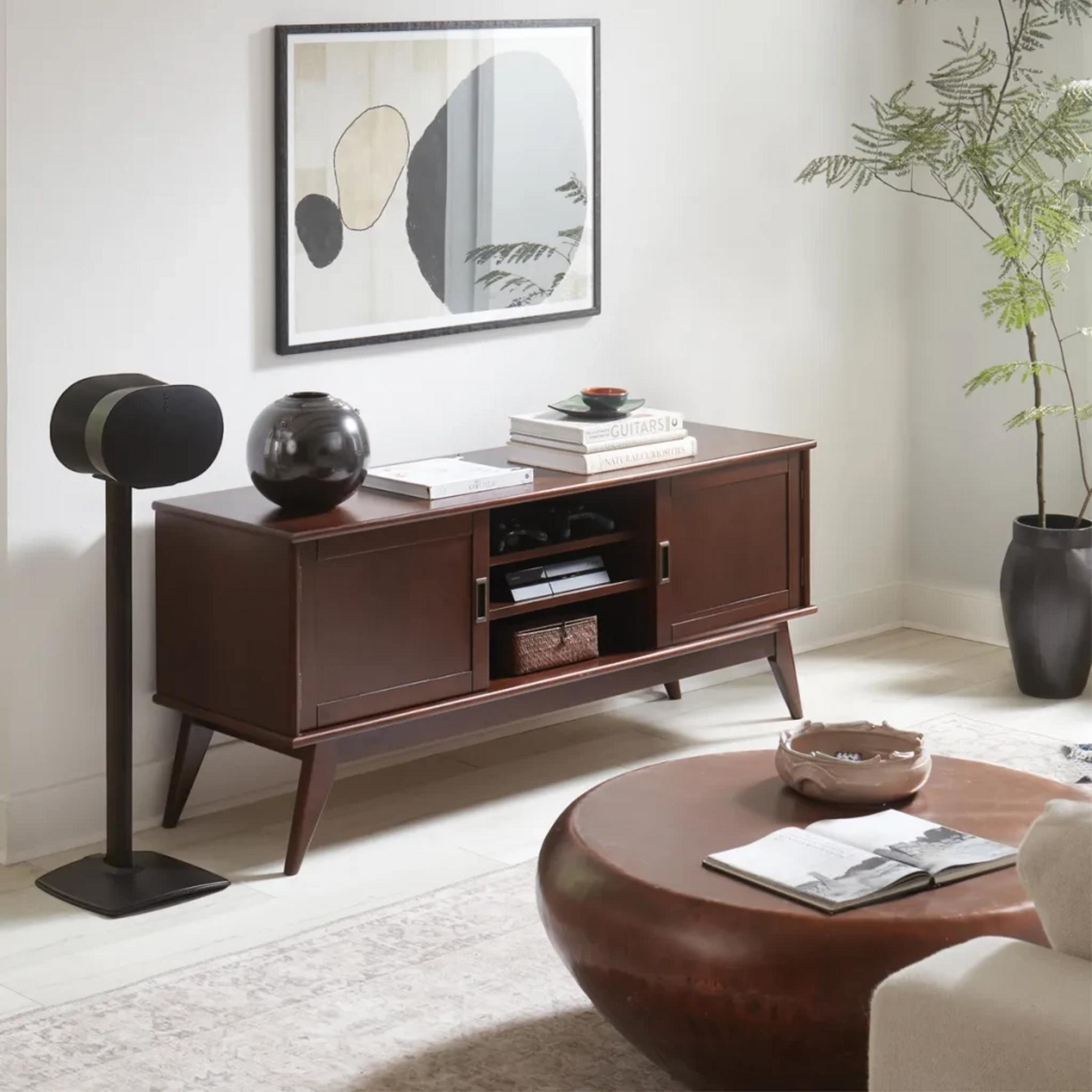 Ein dunkles Holzsideboard mit Kunst und Lautsprechern in einem Wohnzimmer.