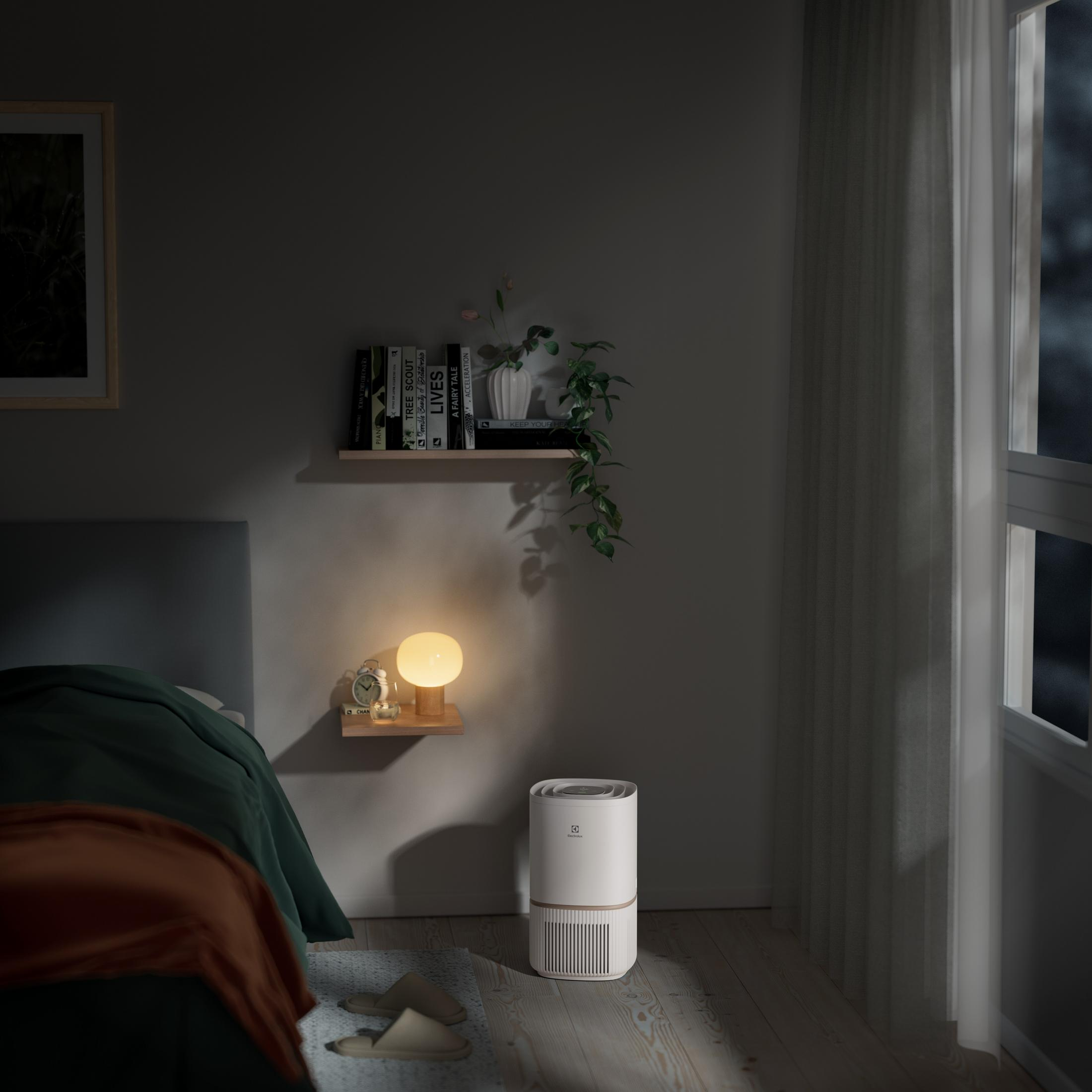 Ein weißer Luftreiniger steht neben einem Bett in einem dunklen Raum mit einem Fenster.