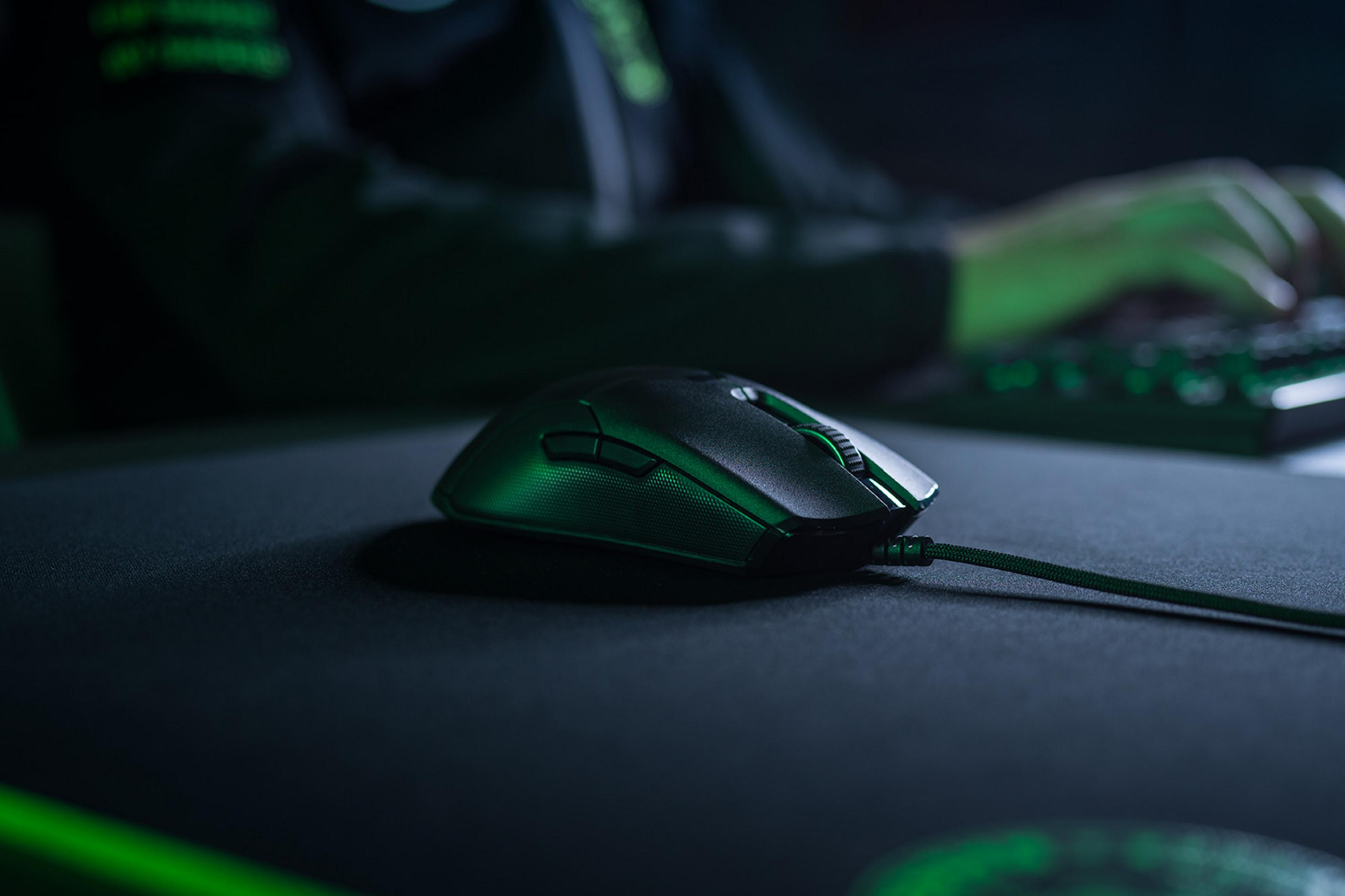 Un mouse da gaming nero con illuminazione verde su un tappetino nero.