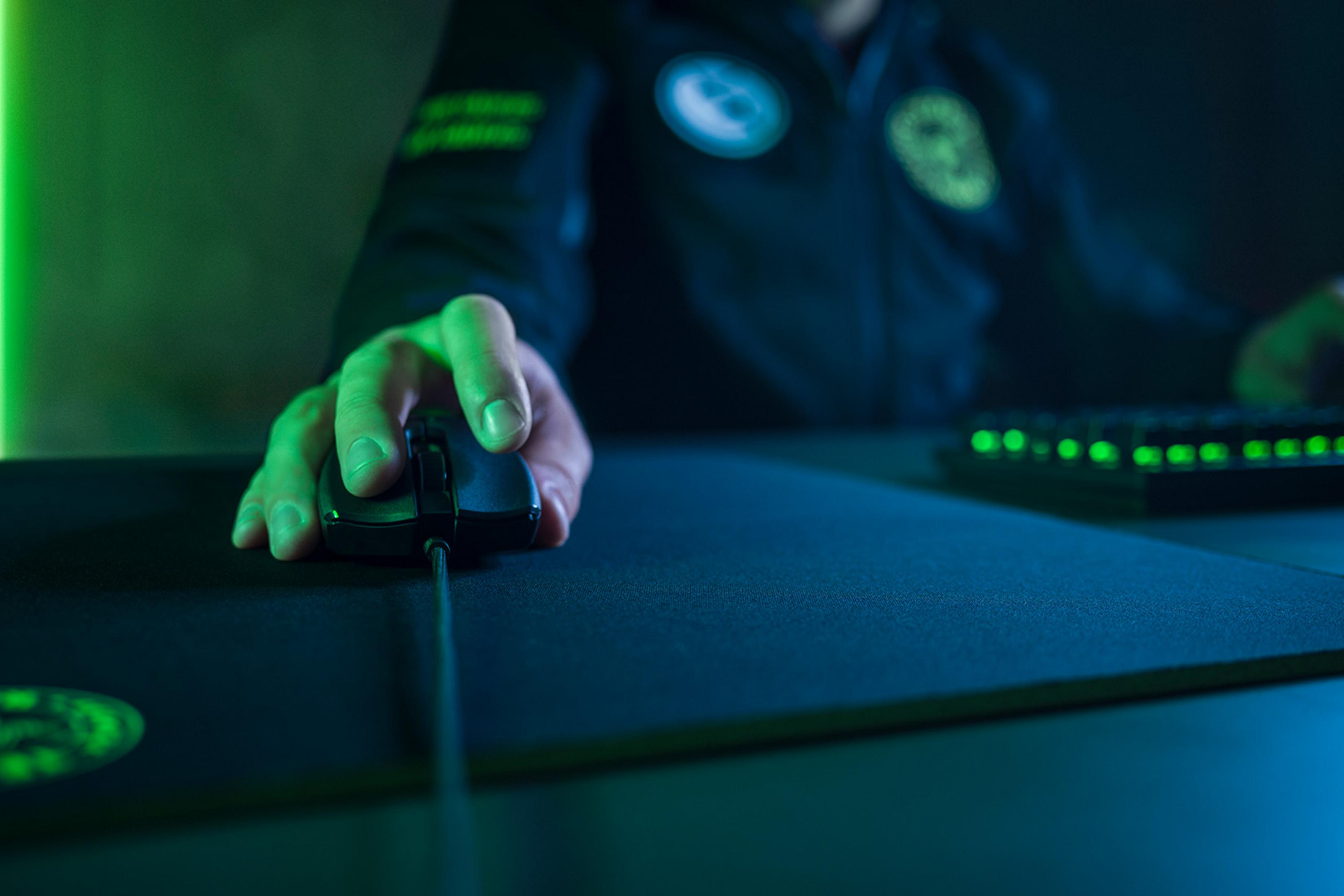Una mano usa un mouse da gaming nero su un tappetino nero.