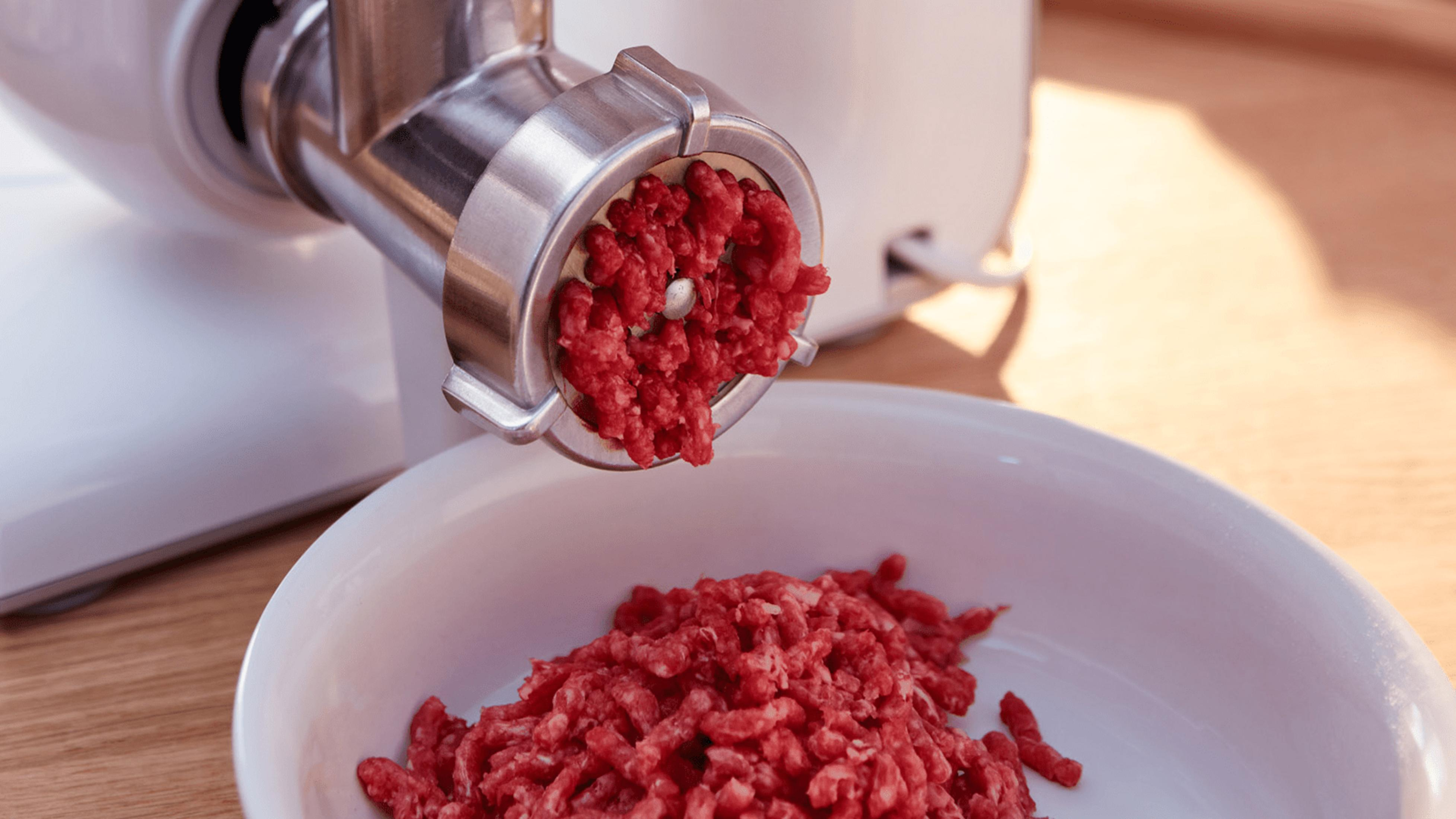 Hackfleisch wird aus einem Fleischwolf in eine weiße Schüssel gefüllt.