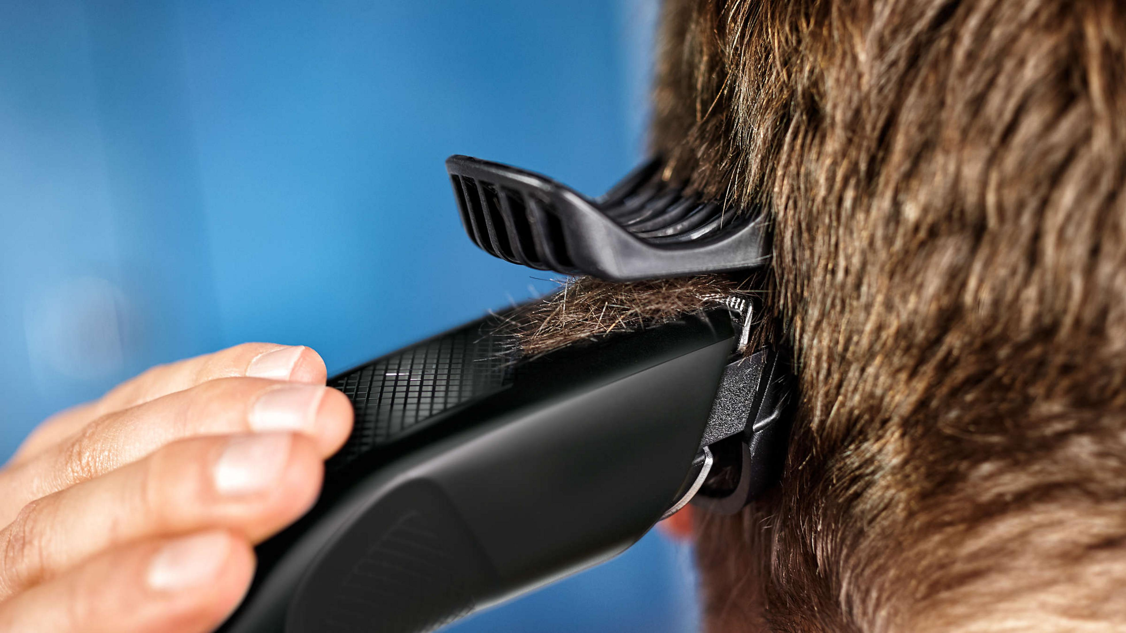 Una mano usa un tagliacapelli nero con pettine su capelli castani.