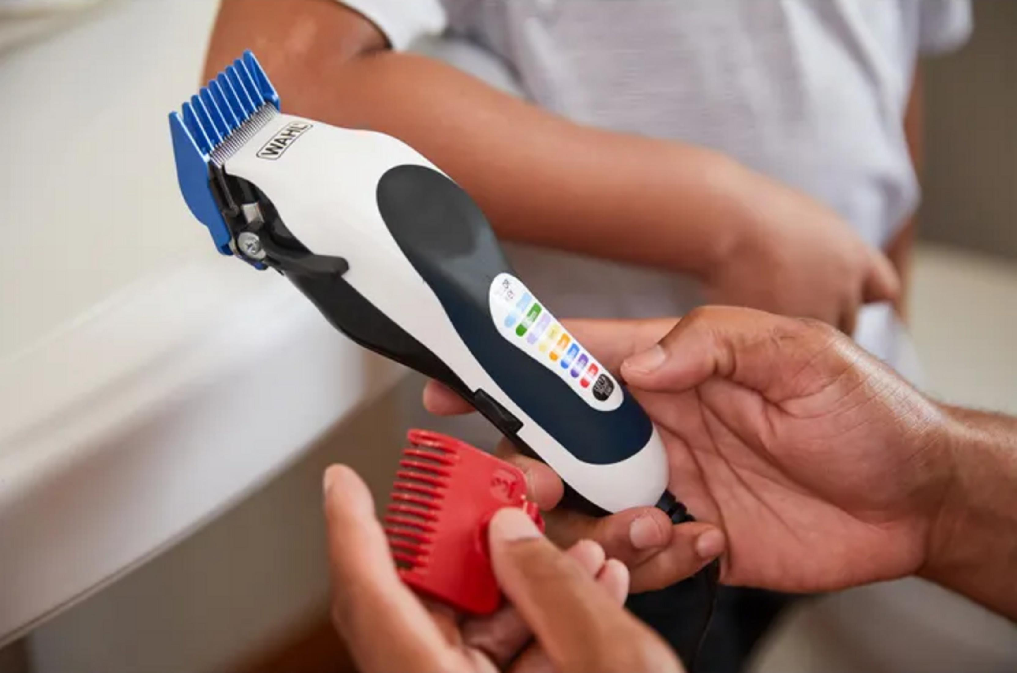 Eine Hand hält einen roten Aufsatz neben einer weißen und blauen Haarschneidemaschine.