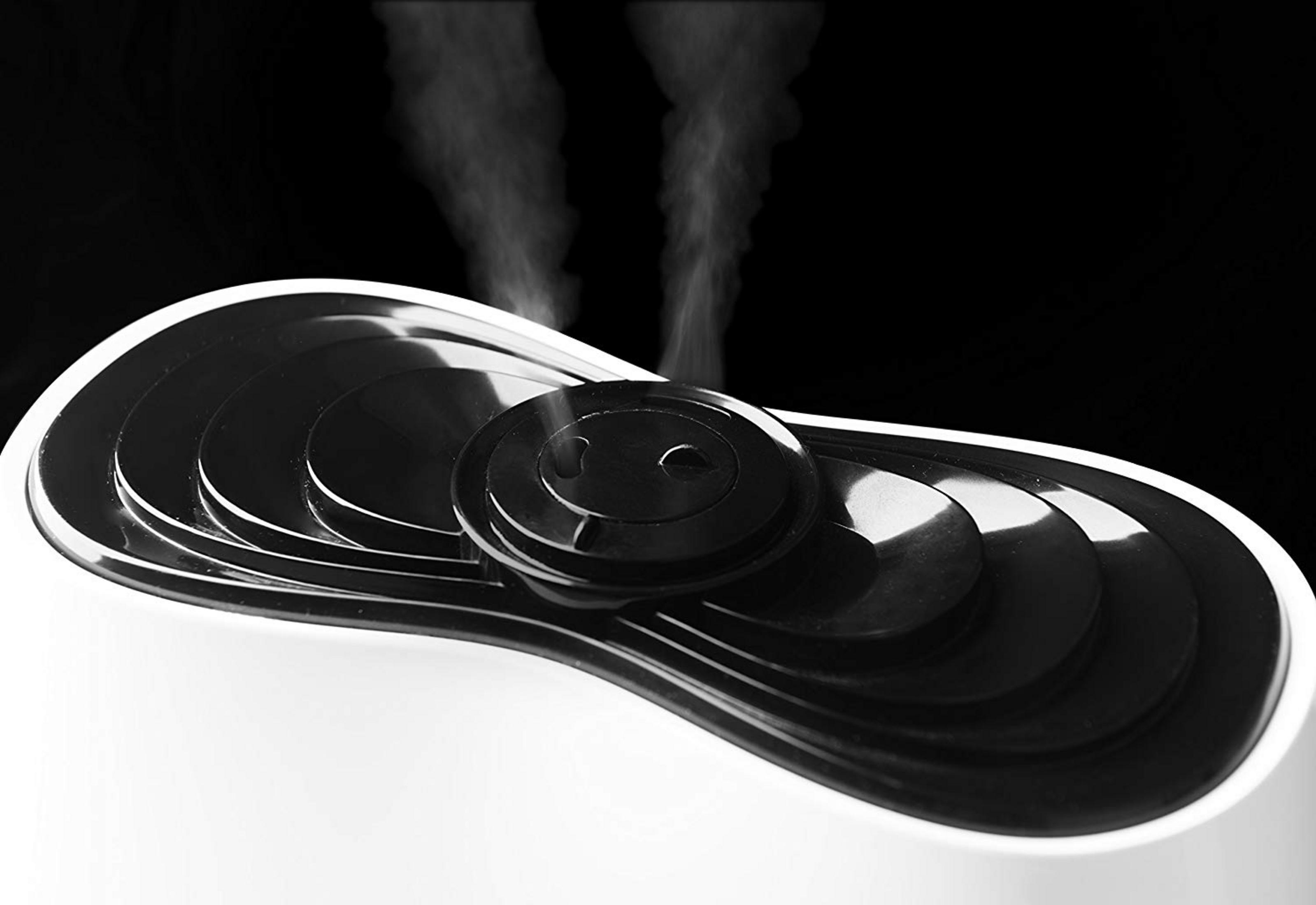 Primer plano de un humidificador blanco con parte superior negra, sale vapor.