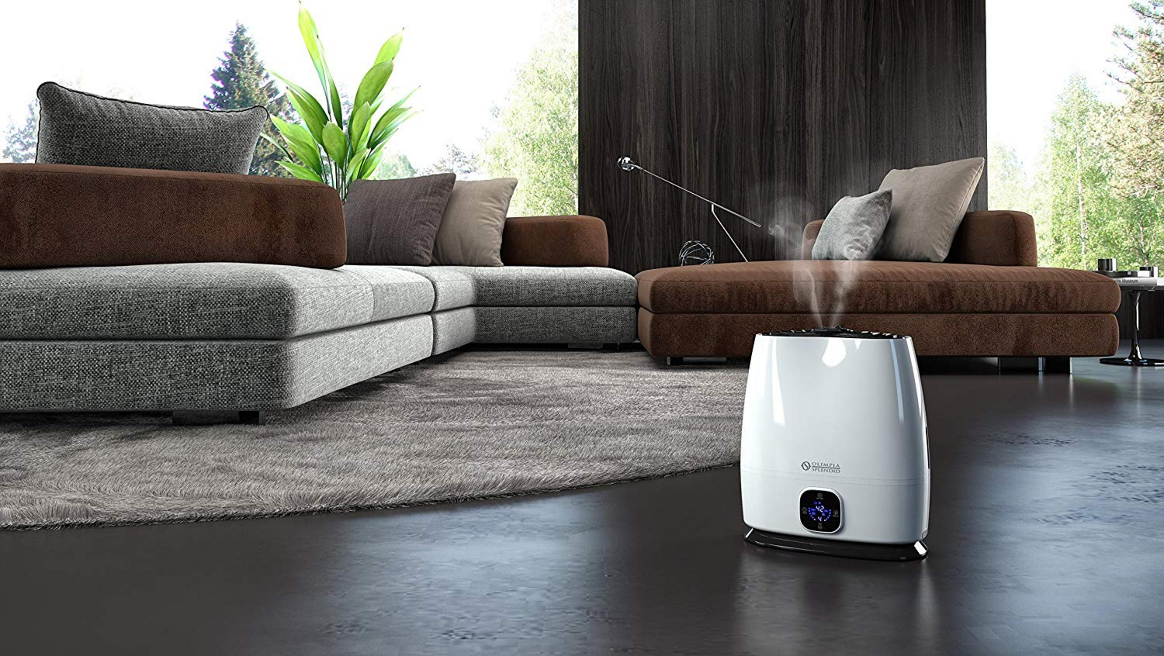 Un humidificador blanco con pantalla azul en suelo oscuro junto a un sofá marrón.