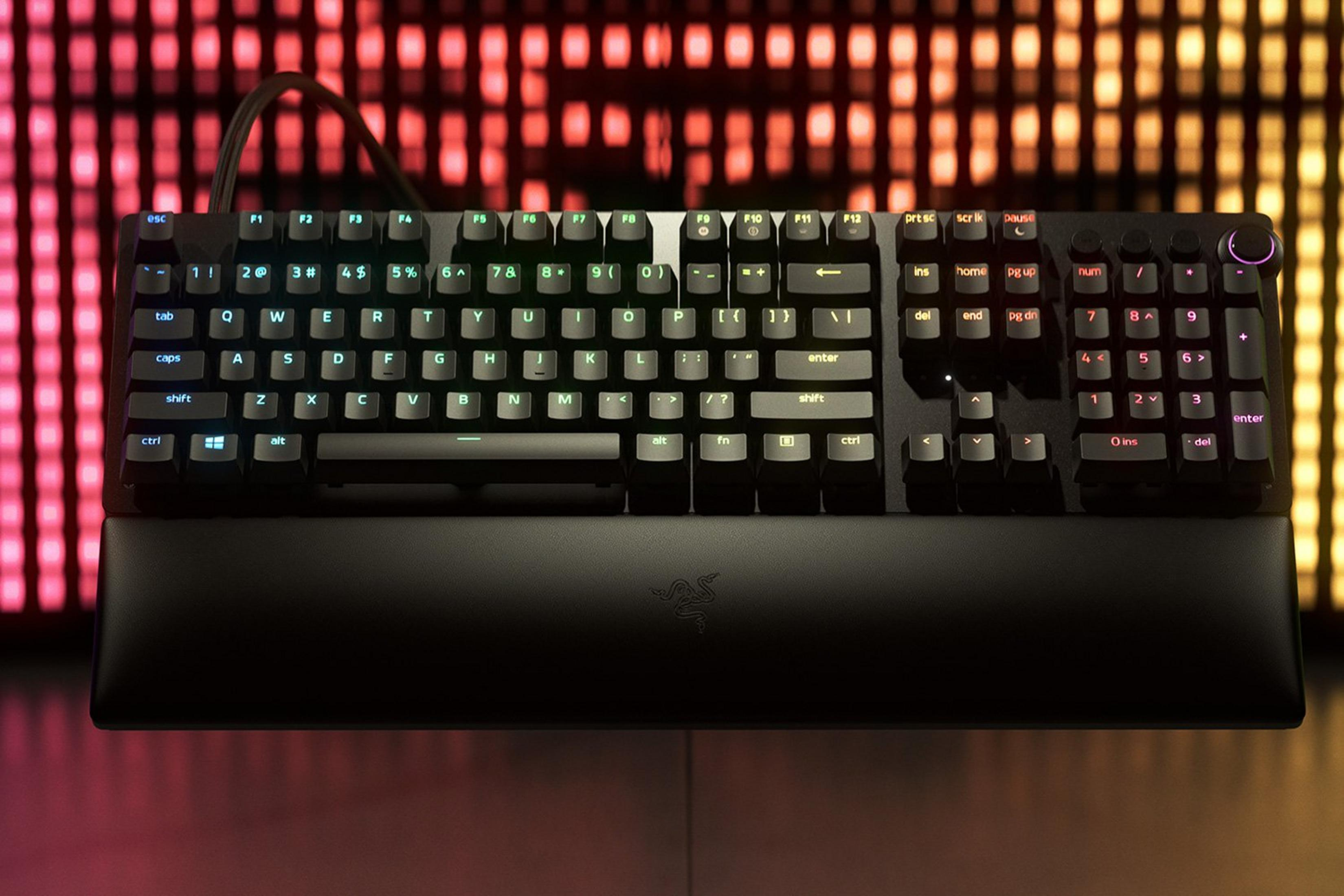 Eine schwarze mechanische Tastatur mit RGB-Beleuchtung vor einem unscharfen, bunten Lichtdisplay.