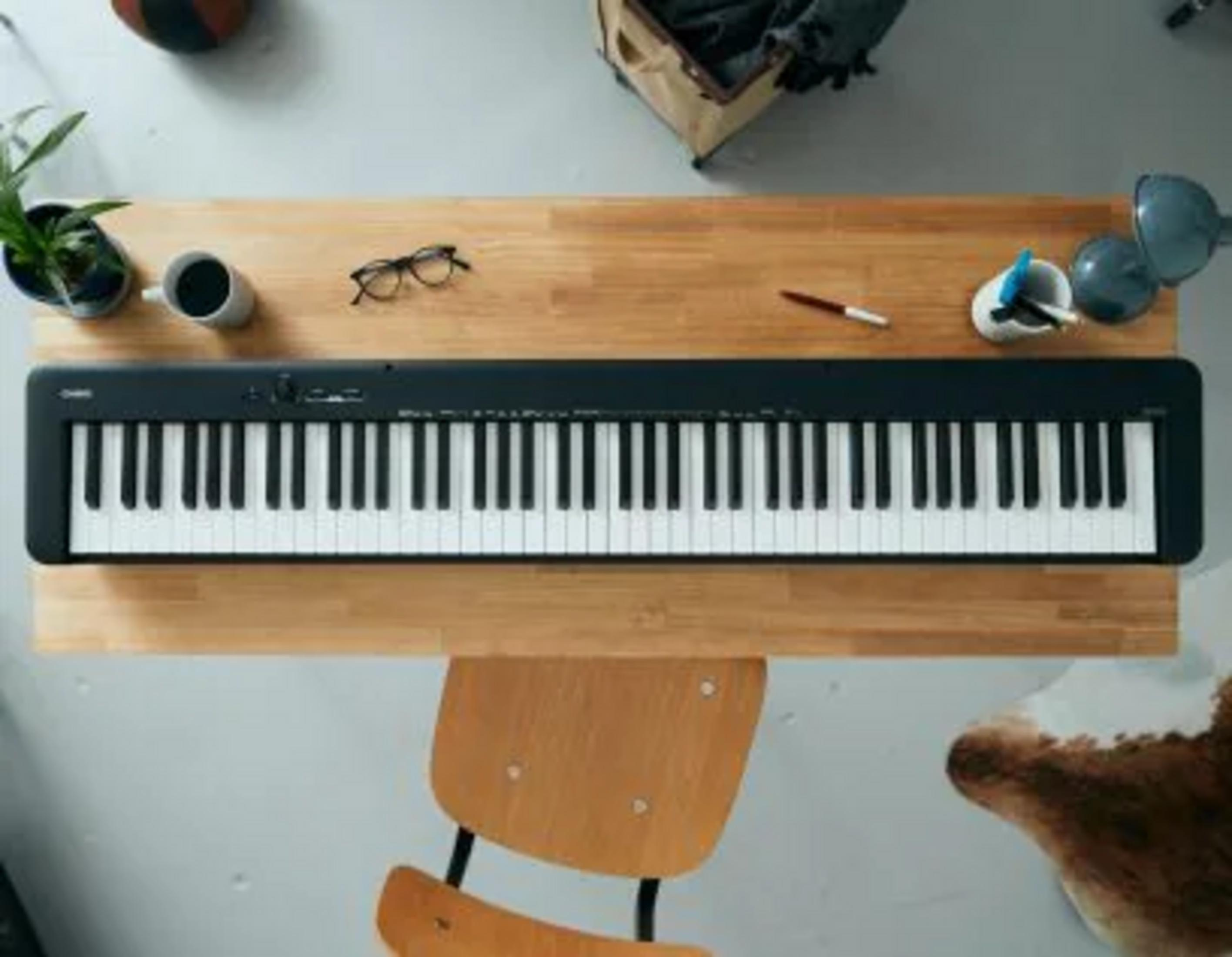 Ein schwarzes Keyboard mit weißen Tasten liegt auf einem Holztisch.