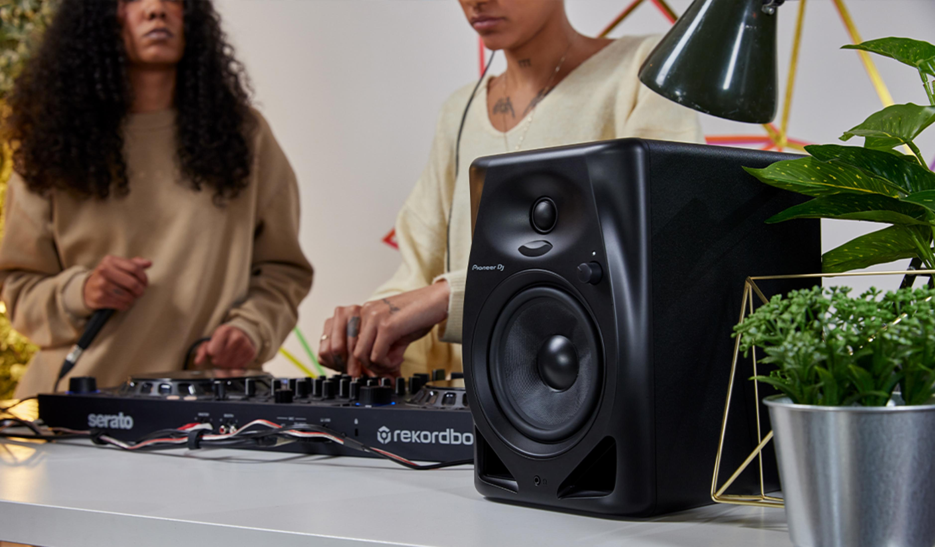 Two DJs are mixing on a console, a black speaker is in the foreground.