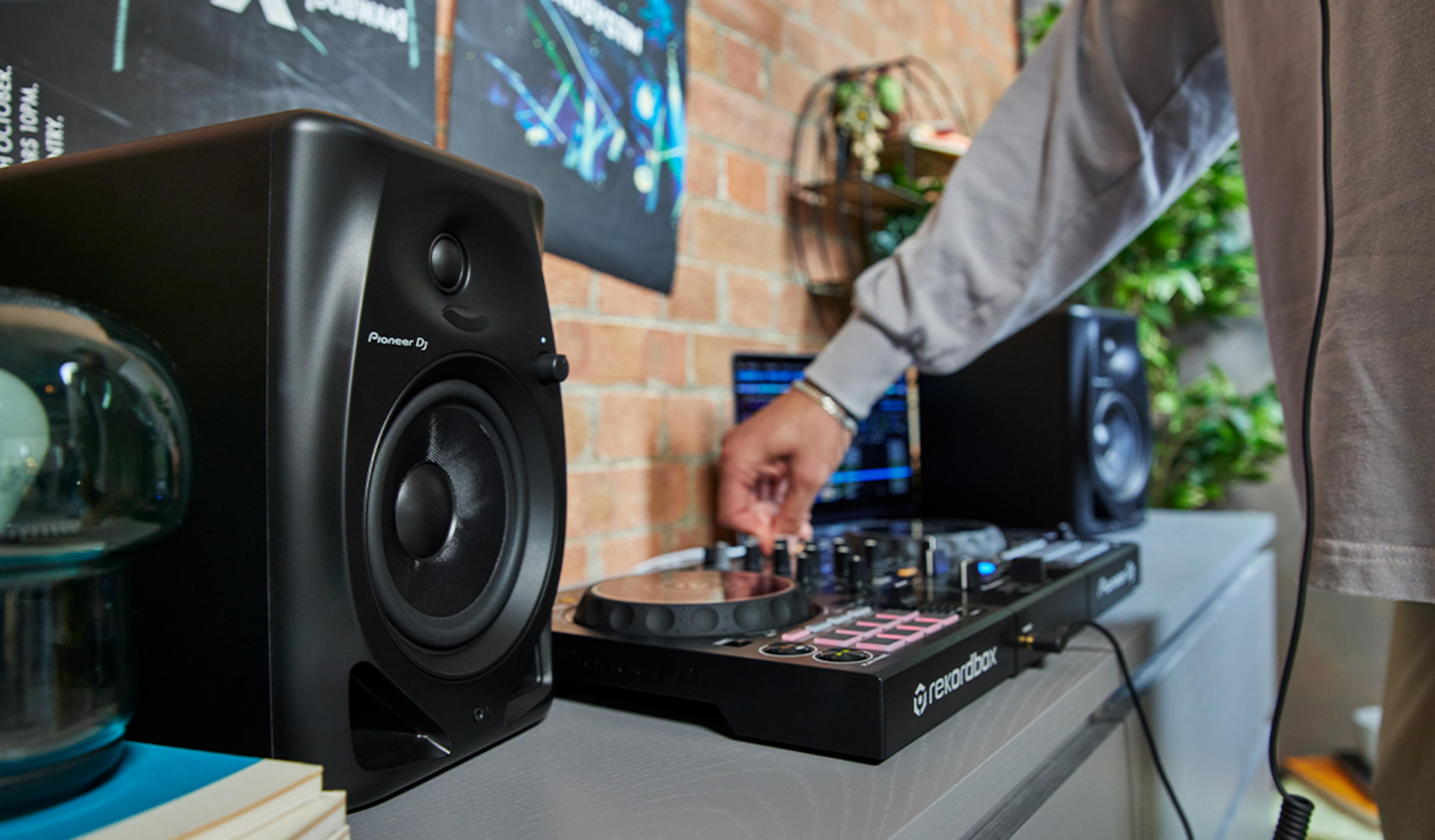 A DJ uses a Pioneer DJ controller with a laptop and two speakers.