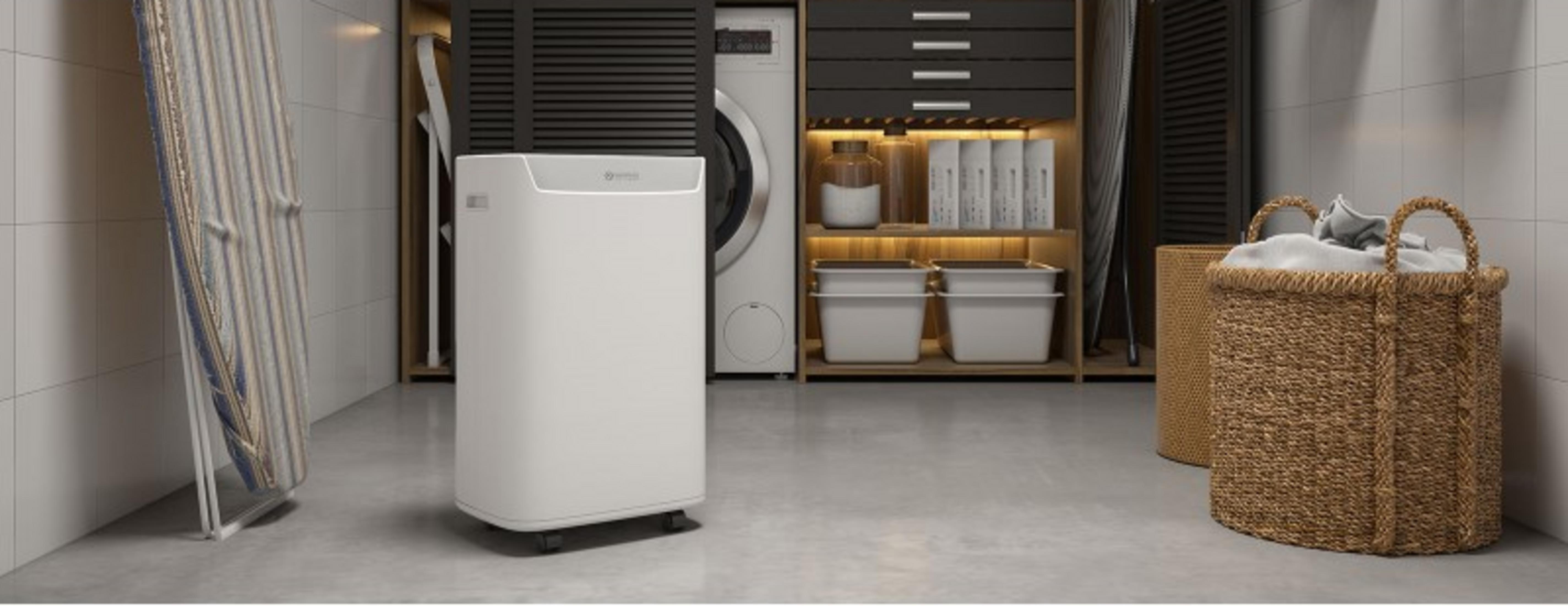 Biały oczyszczacz powietrza obok pralki, kosza i deski do prasowania.