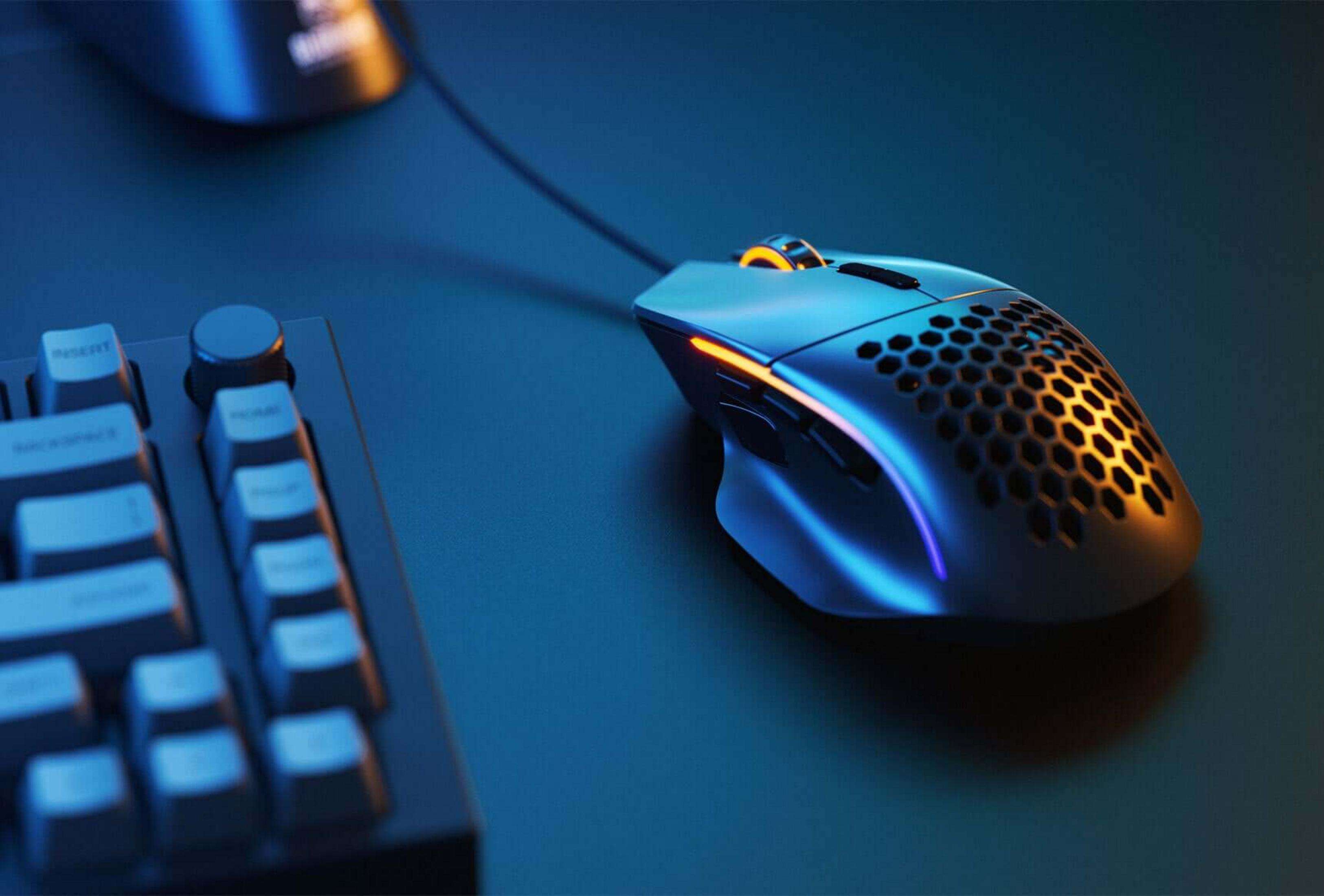 Un mouse da gaming a nido d'ape con illuminazione RGB accanto a una tastiera.