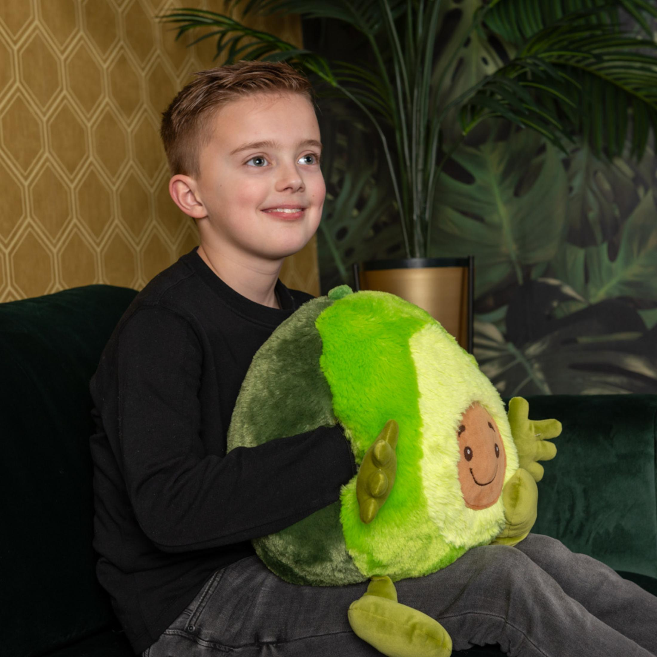 Ein Junge sitzt auf einem grünen Sofa und hält ein Avocado-Kissen.