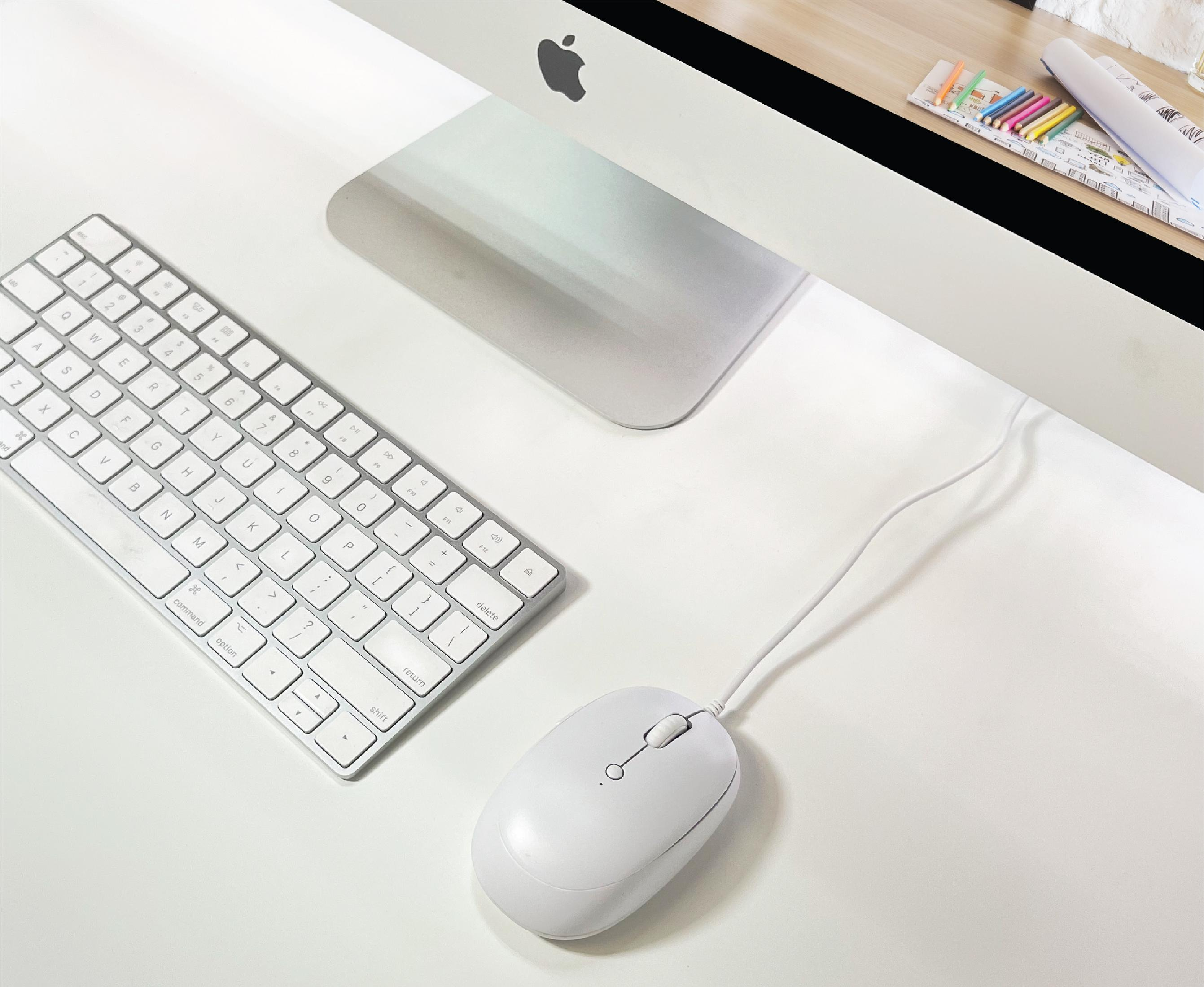 Un teclado y ratón blancos de Apple sobre un escritorio blanco junto a un iMac.