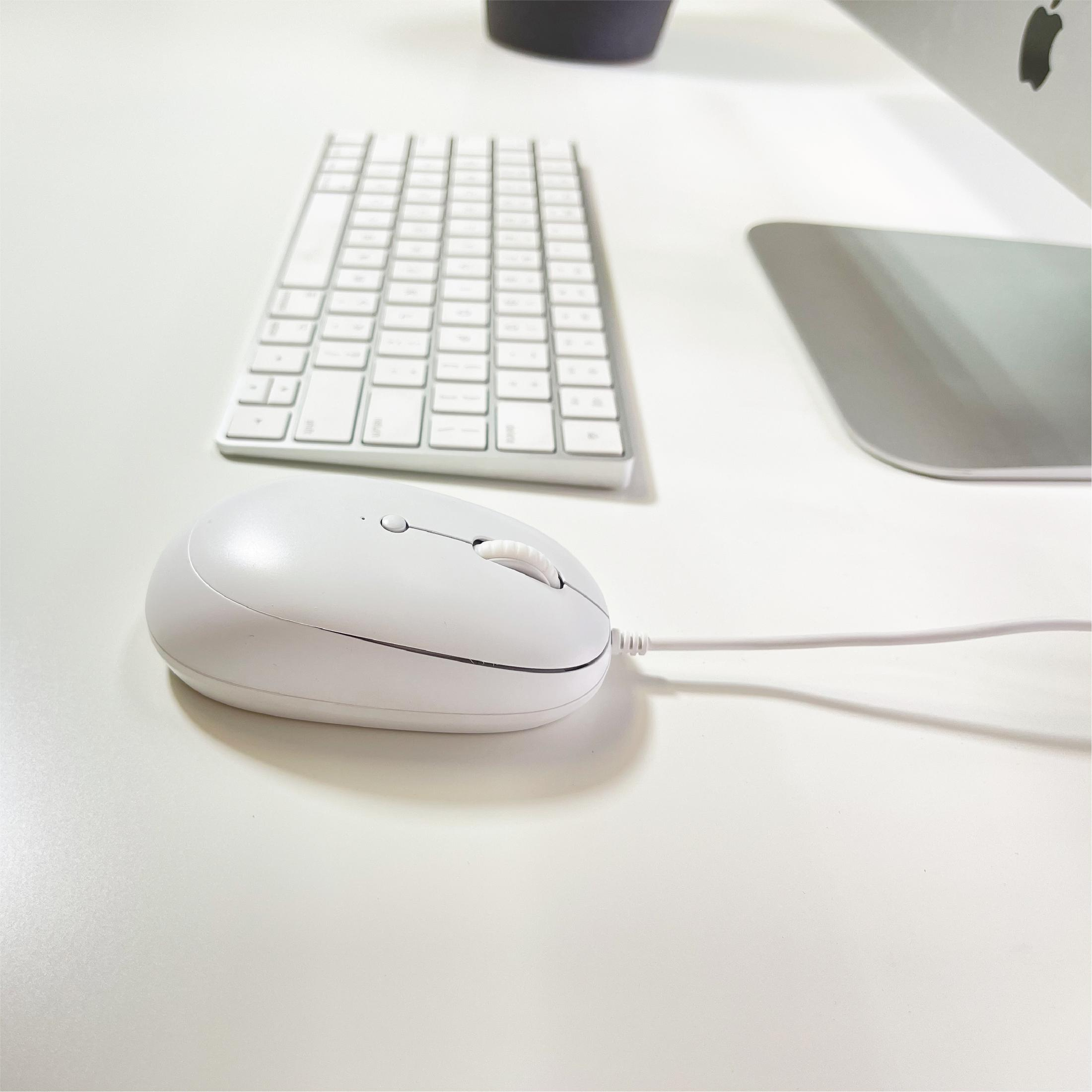 Un ratón y teclado blancos están sobre un escritorio blanco, junto a parte de un monitor.