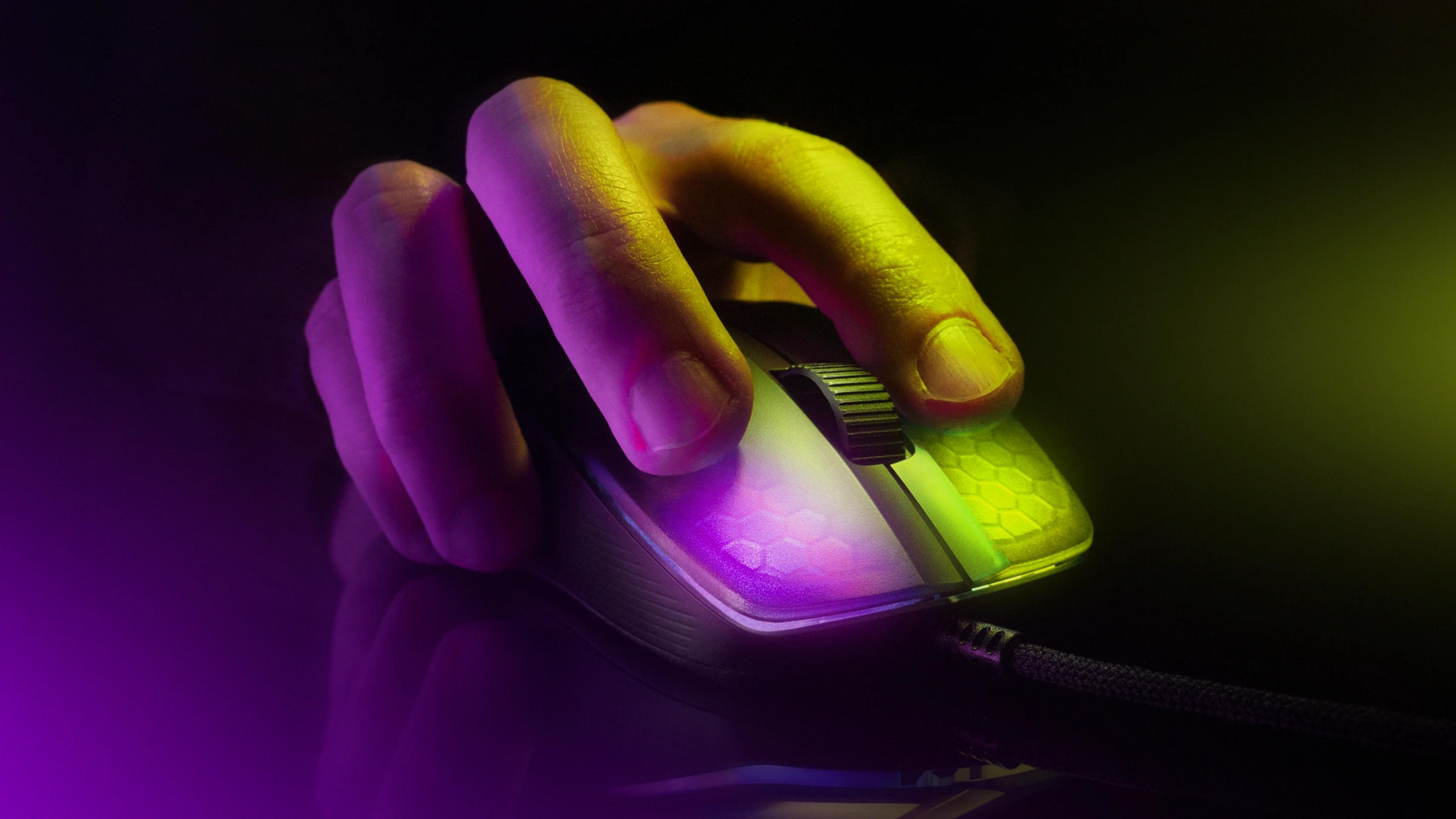Una mano agarra un ratón de ordenador iluminado con luz púrpura y amarilla.