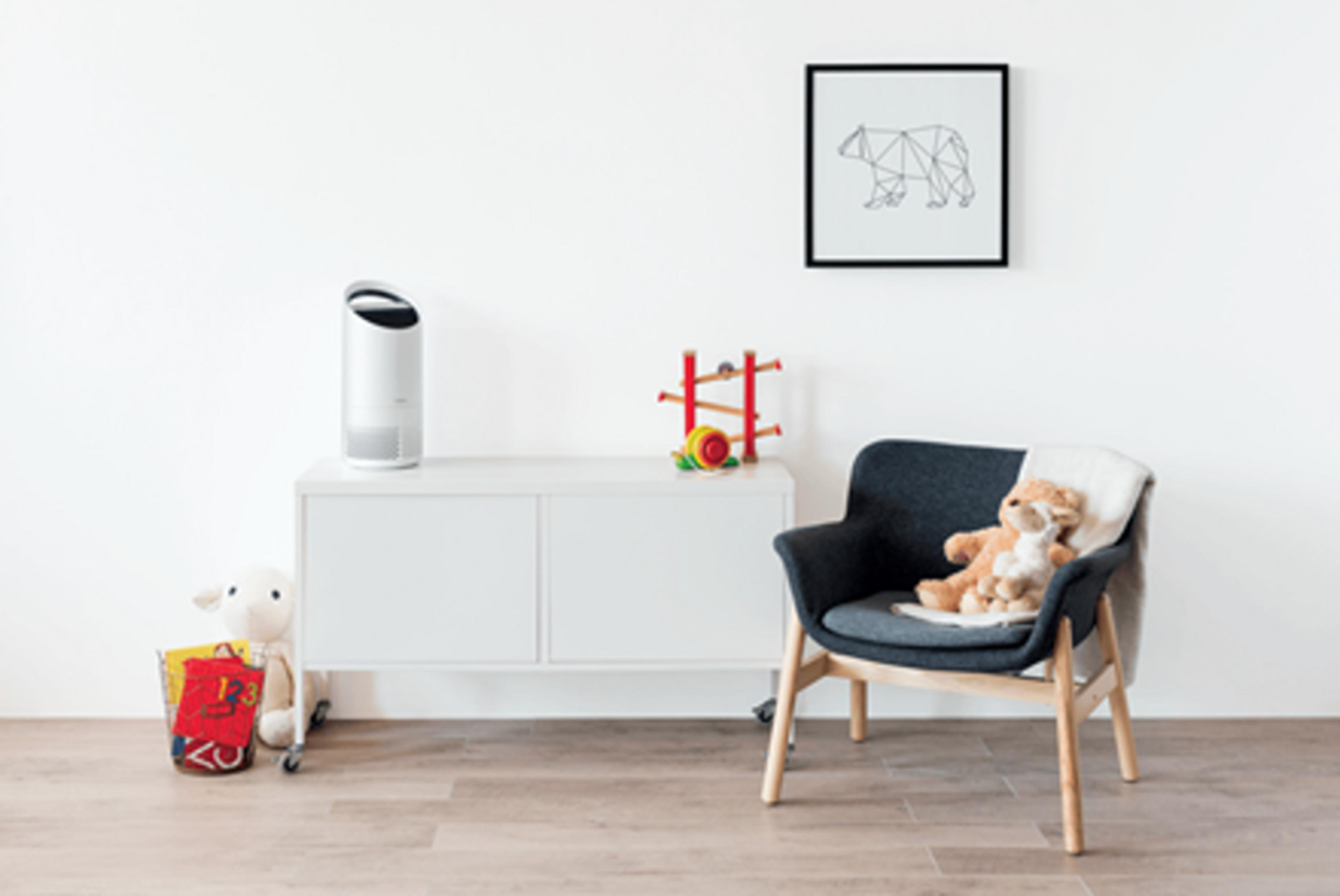 Ein weißer Luftreiniger auf einem Schrank, daneben Spielzeug und ein Sessel mit Teddybär.