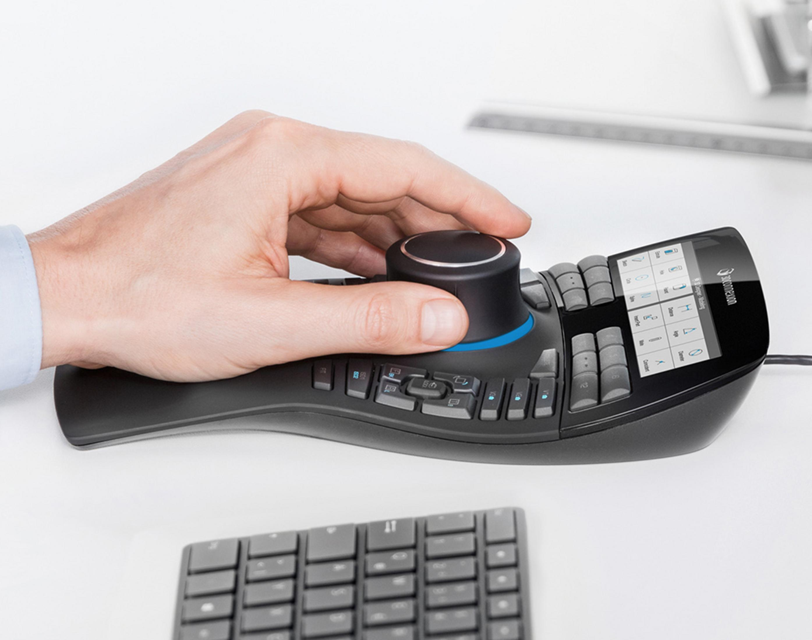 A hand operates a black 3D mouse with a dial and screen.