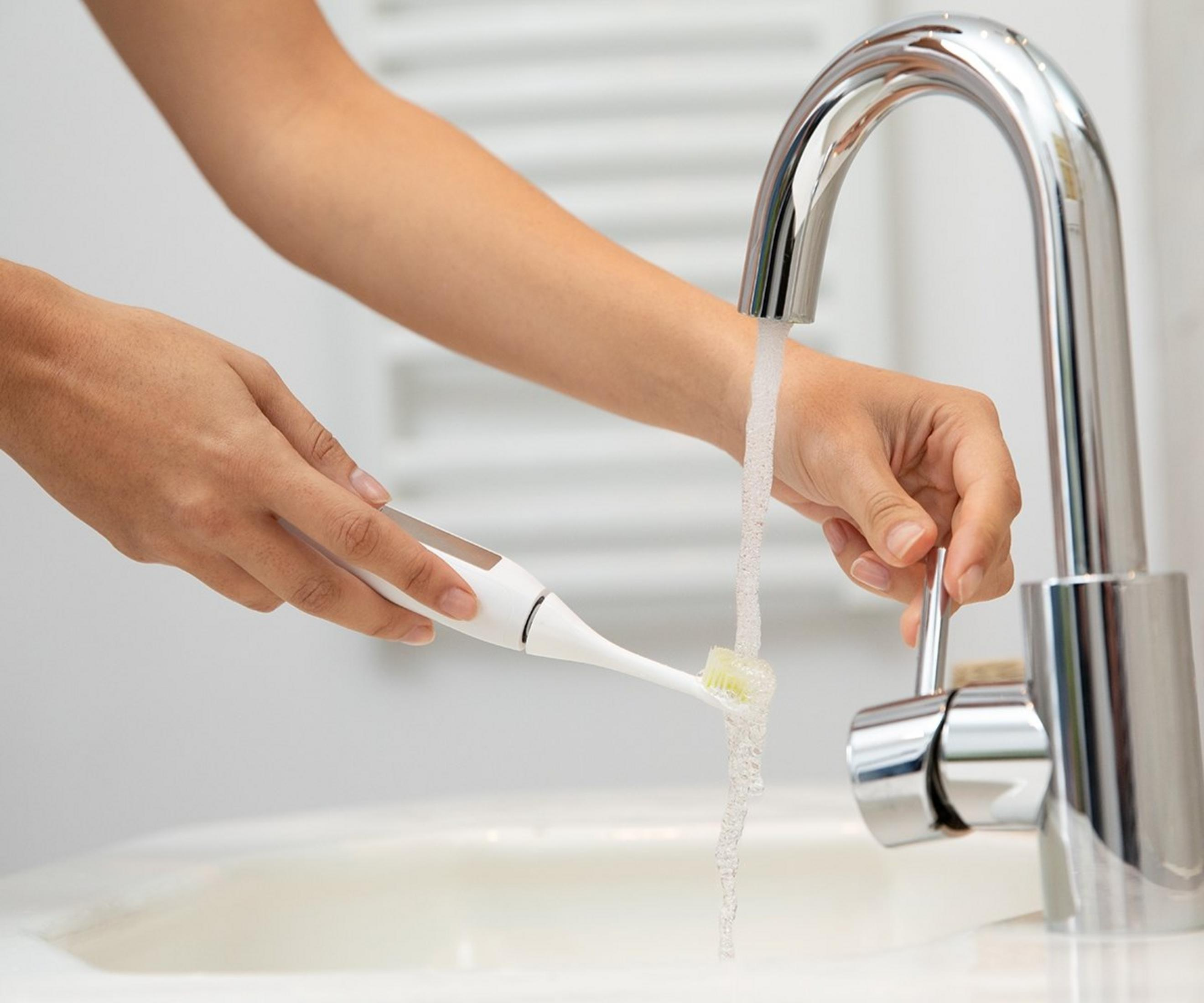 Personne rinçant une brosse à dents électrique sous l'eau courante.