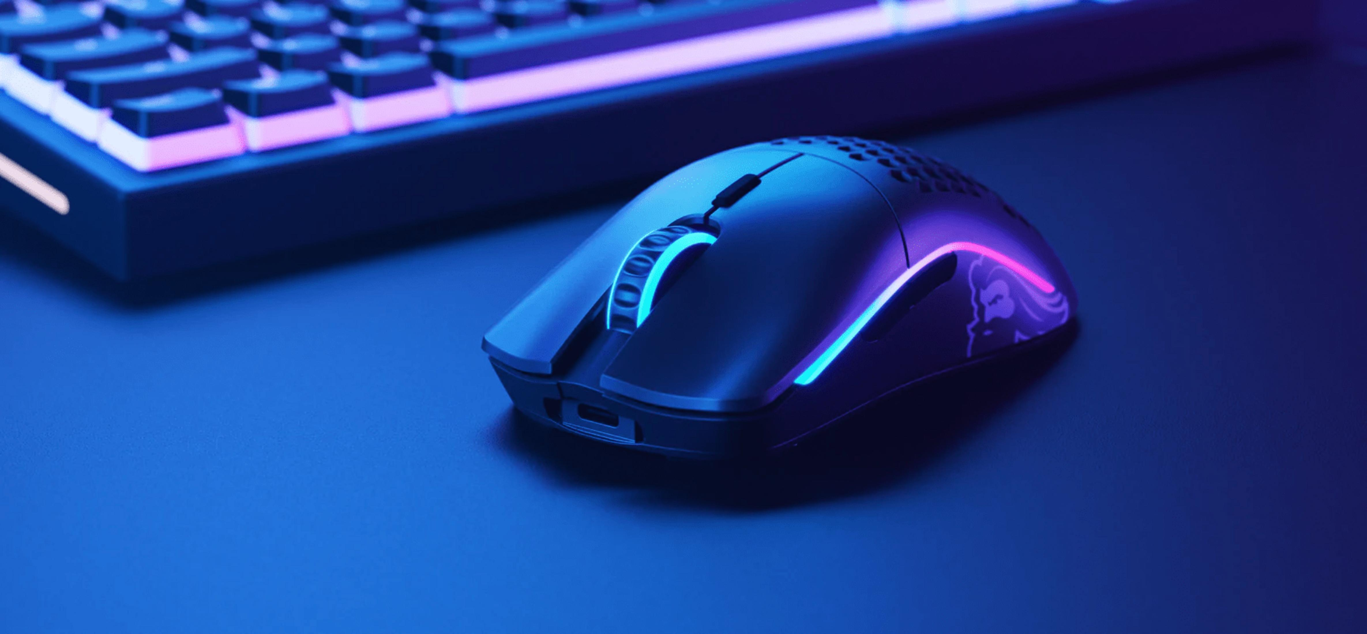 Czarna mysz gamingowa z niebieskim i różowym podświetleniem obok klawiatury.