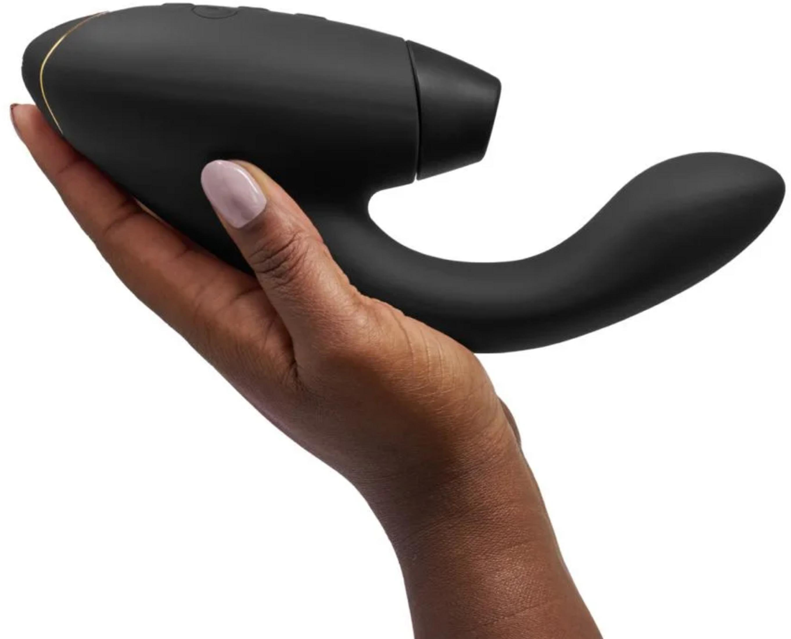 Eine Hand hält einen schwarzen, geschwungenen Vibrator mit goldener Zierleiste.