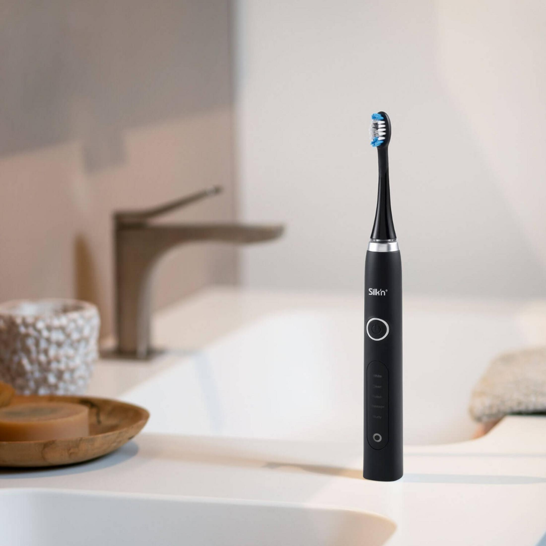 Czarna szczoteczka elektryczna z niebieskim włosiem stoi na białej umywalce.