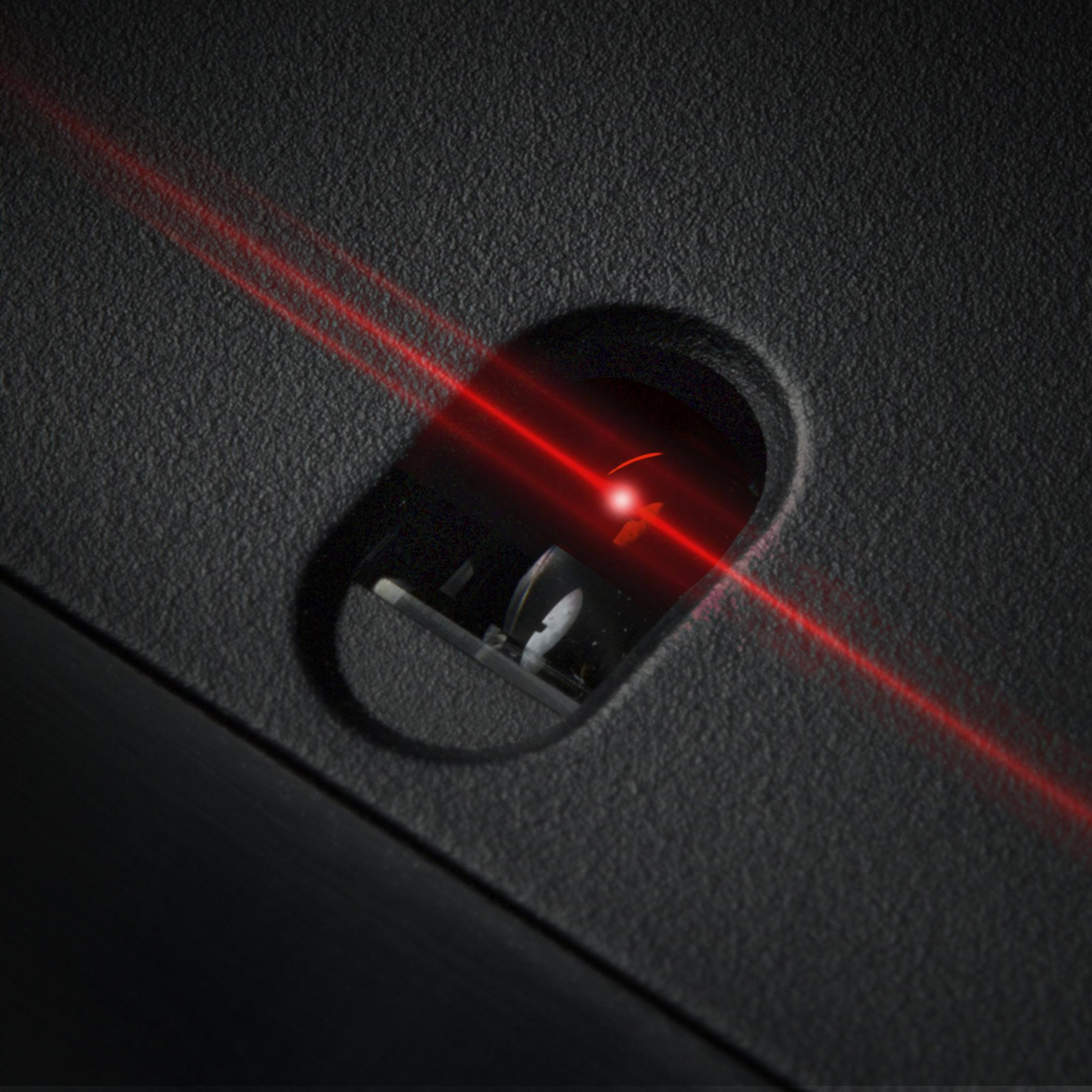 Czerwona wiązka lasera migocze na czarnej, teksturowanej powierzchni i czujniku optycznym.