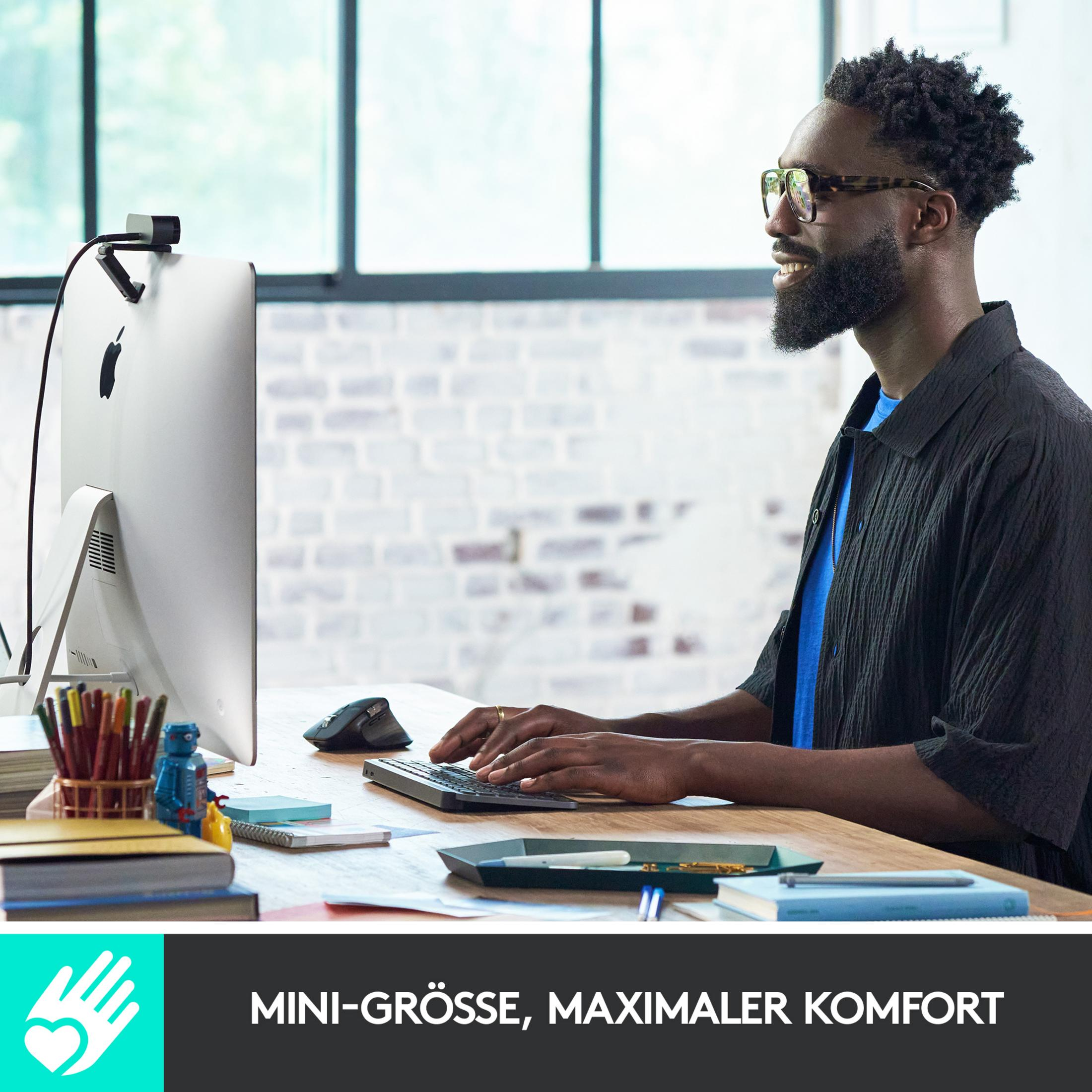 Mężczyzna w okularach pisze na klawiaturze przed iMac z kamerą.