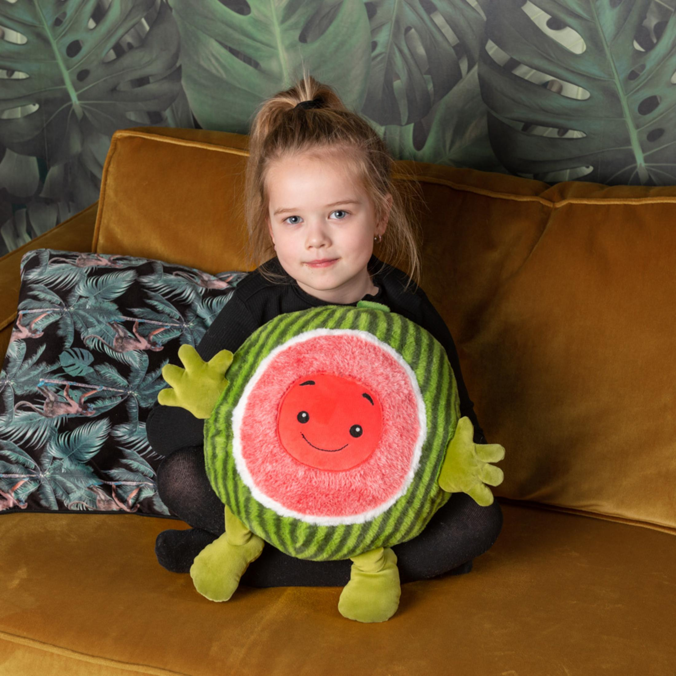 Ein junges Mädchen sitzt auf einem braunen Sofa und hält ein Wassermelonen-Kuscheltier.