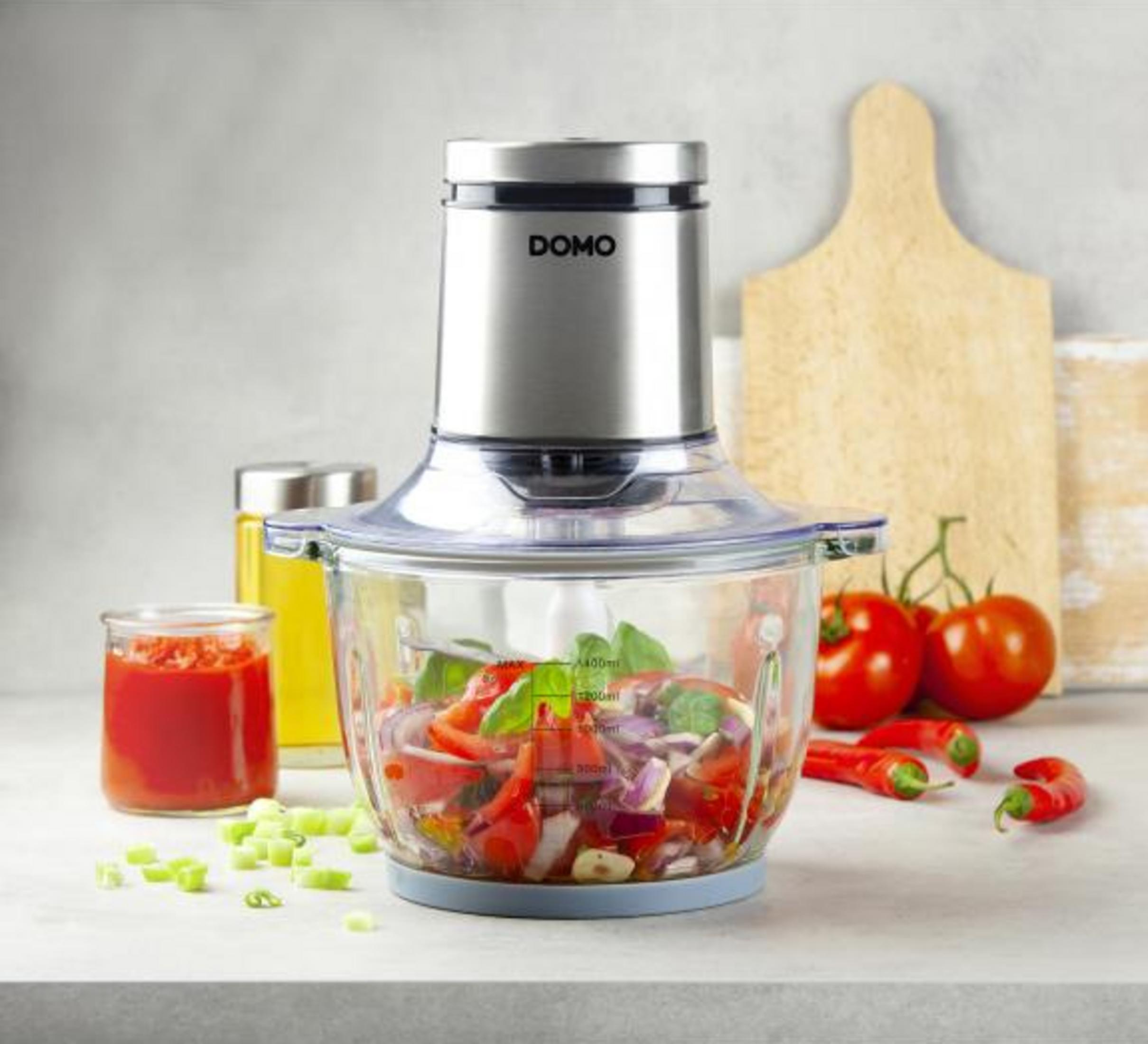 Un robot da cucina con cipolle, pomodori ed erbe. Pomodori e peperoncini nelle vicinanze.