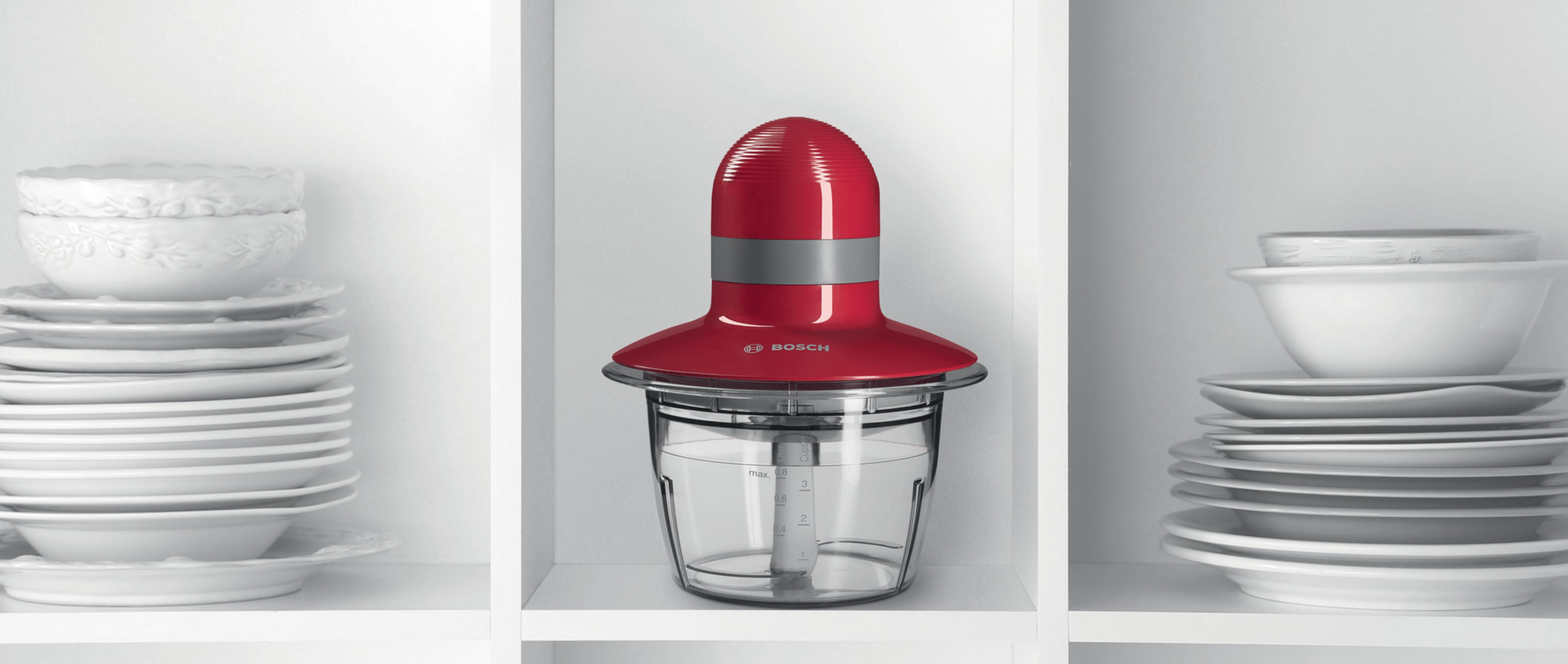 Un procesador de alimentos Bosch rojo se encuentra entre pilas de platos y cuencos blancos.