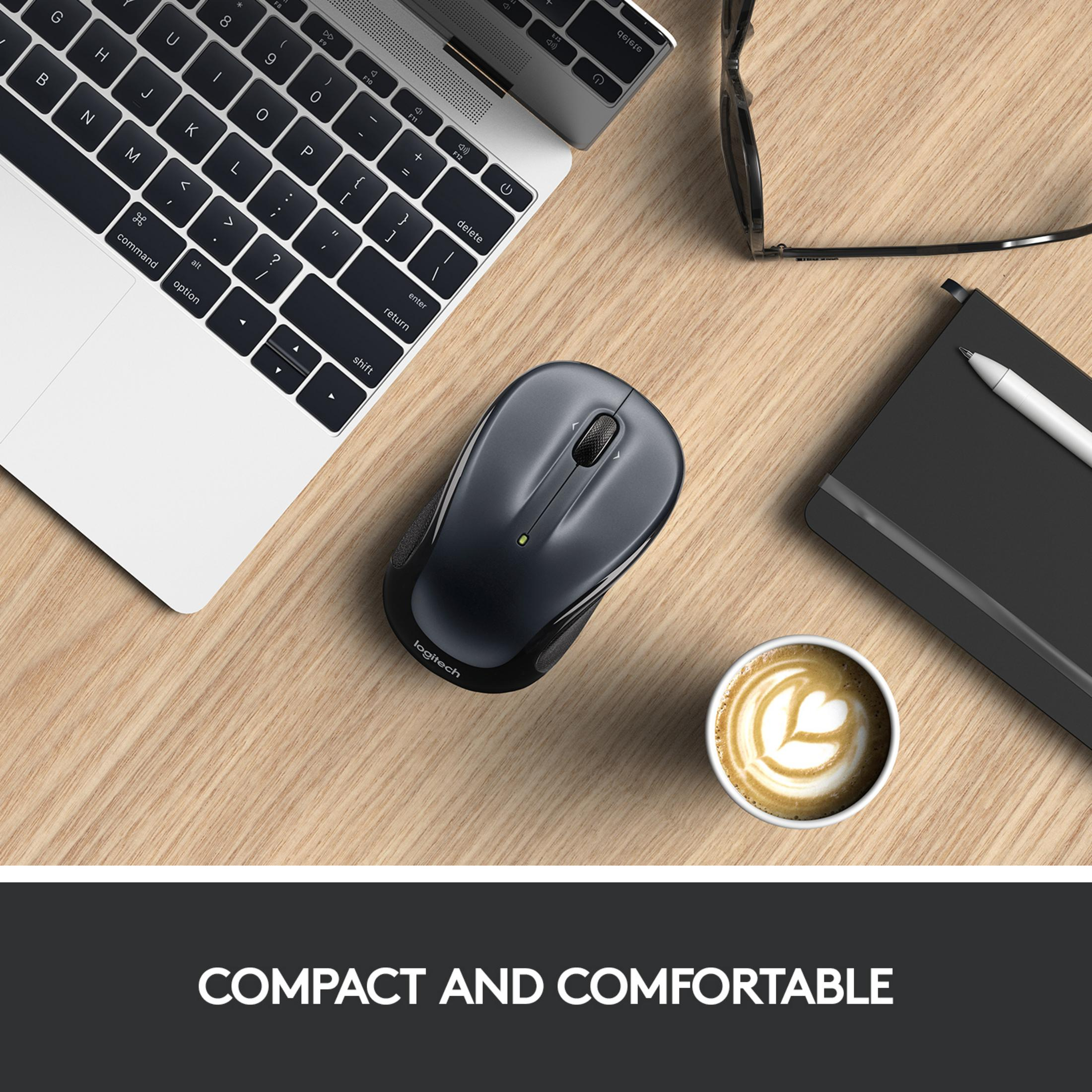 Eine schwarze Logitech-Maus liegt neben einem Laptop, Kaffee und Brille auf einem Holztisch.