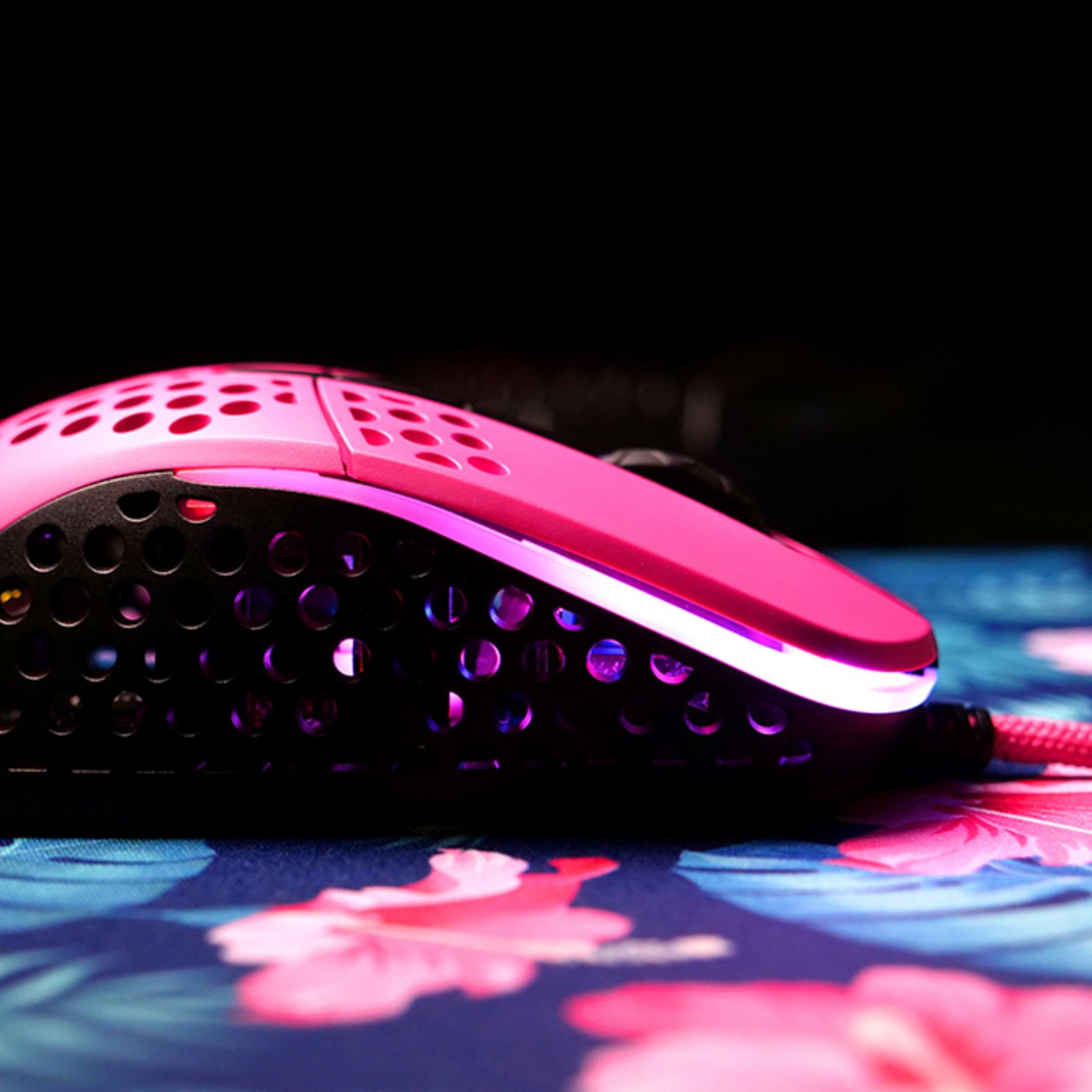 A pink gaming mouse with a hole pattern and purple lighting on a colorful mat.