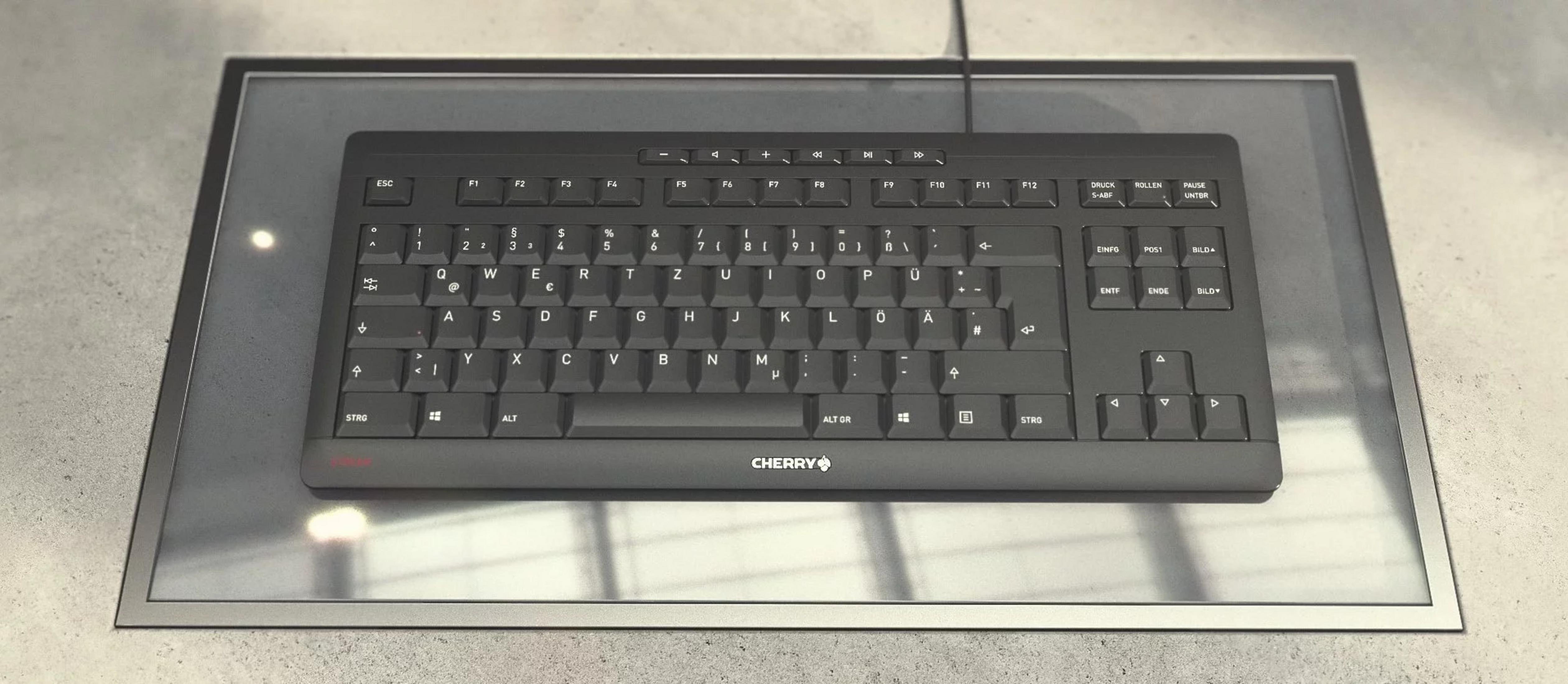 Eine schwarze Cherry-Tastatur liegt auf einer Glasplatte über einem grauen Untergrund.