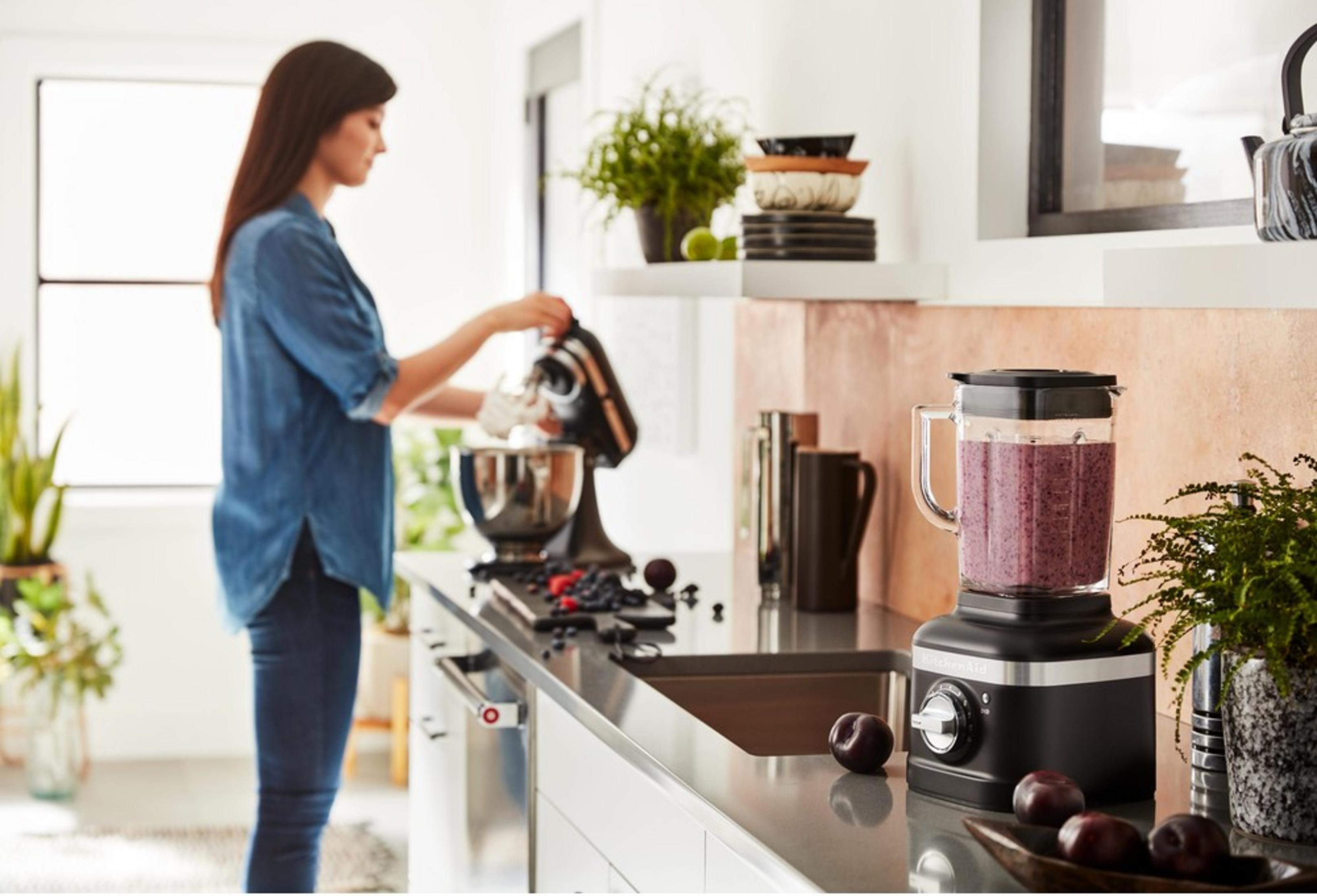 Eine Frau bereitet einen Smoothie zu, während ein Mixer auf der Küchentheke steht.