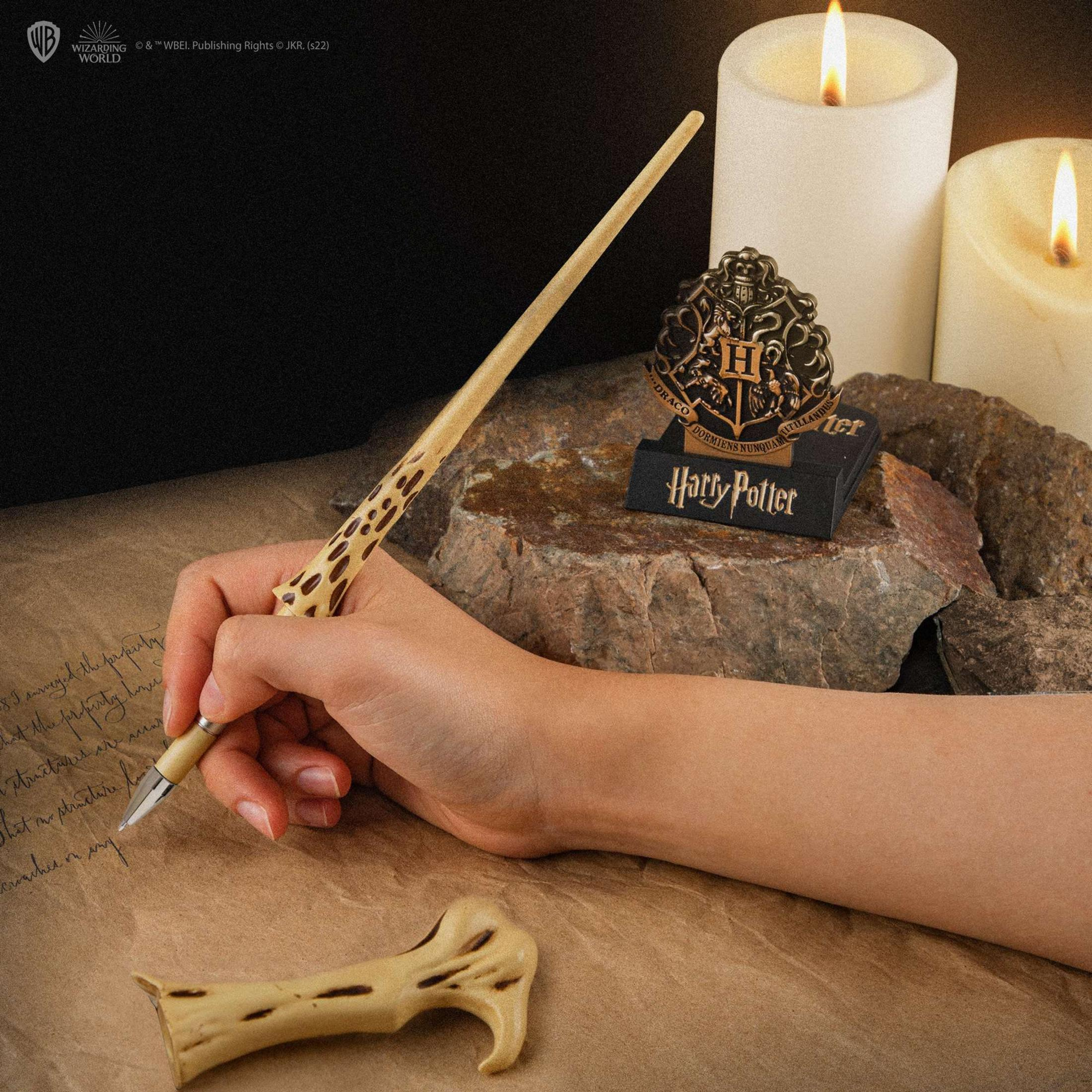 Una mano tiene una bacchetta su pergamena, candele e decorazioni di Harry Potter.