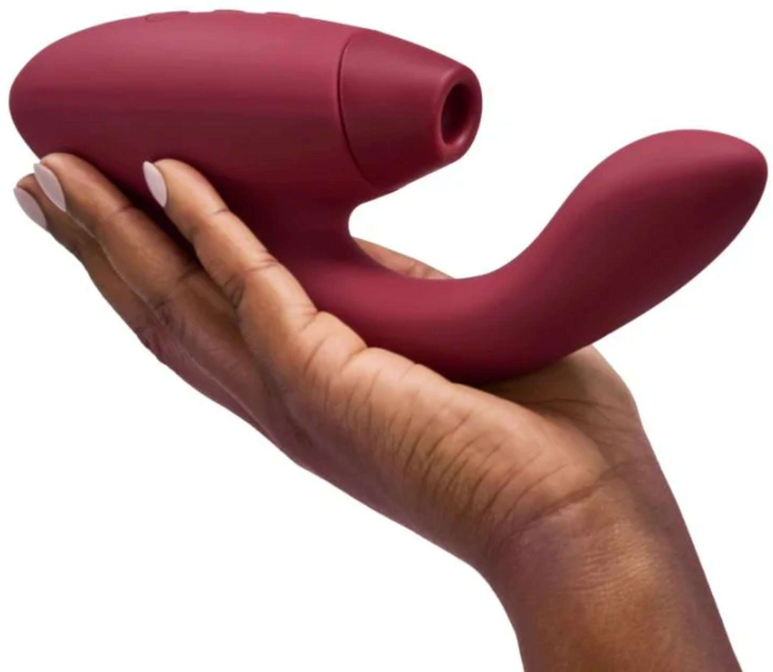 Una mano sostiene un vibrador burdeos con forma curva y apertura redonda.