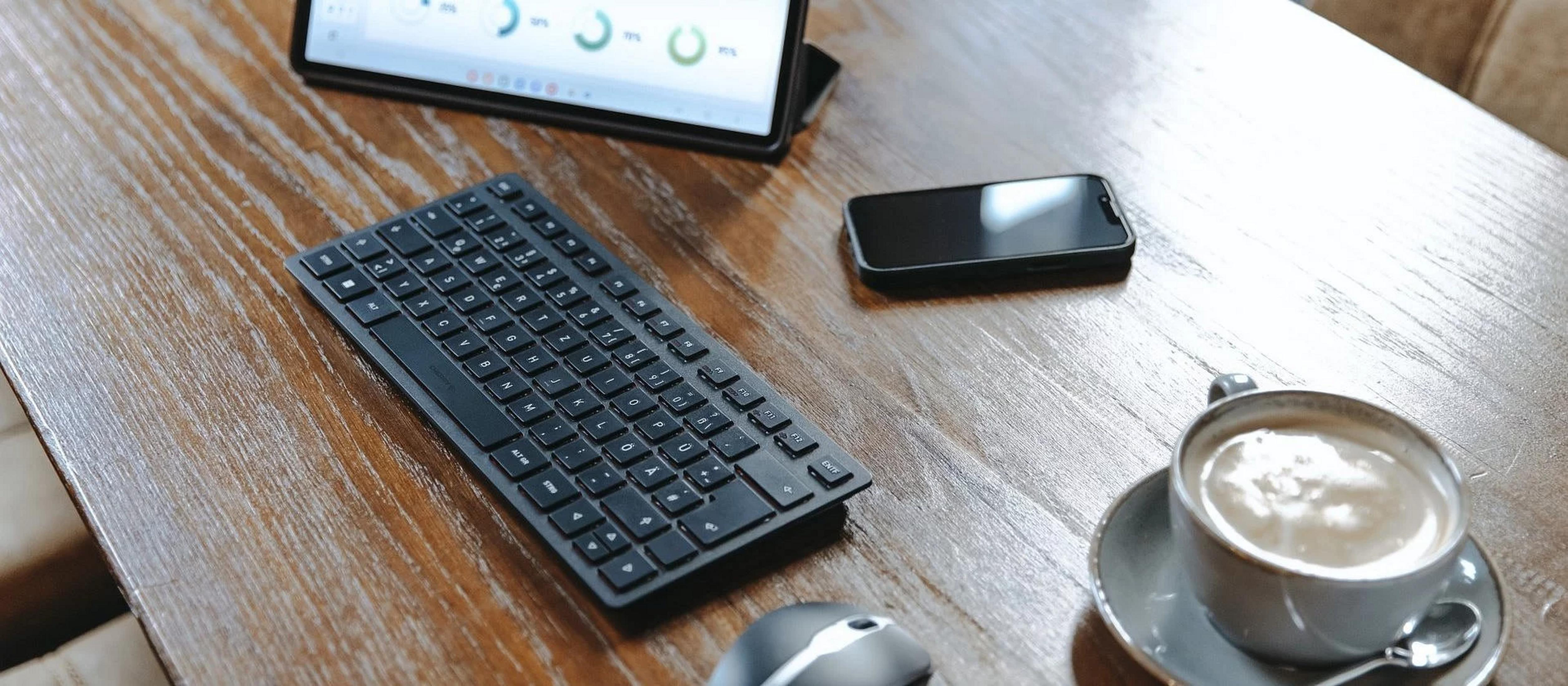 Tastiera nera, mouse, smartphone e caffè su tavolo di legno.
