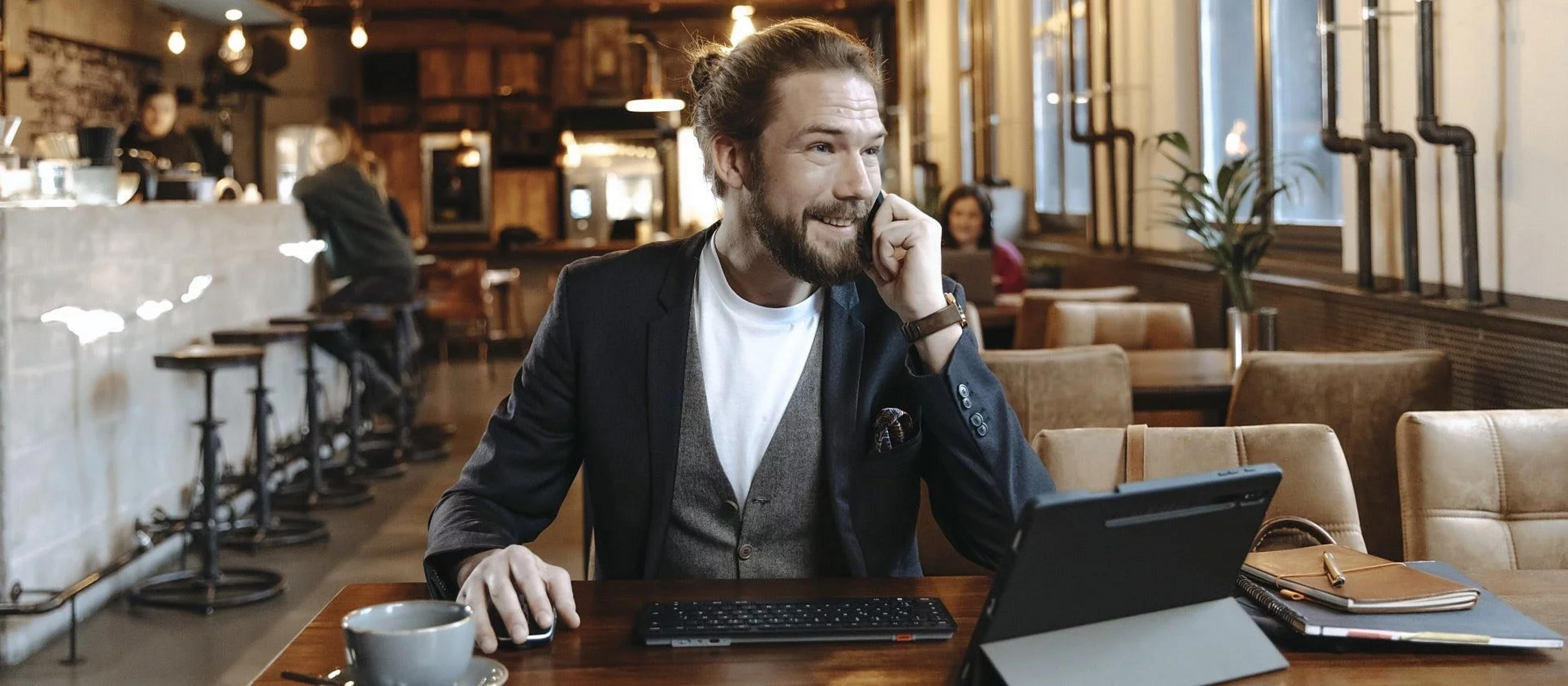 Un uomo con uno chignon parla al telefono a un tavolo con laptop e mouse.