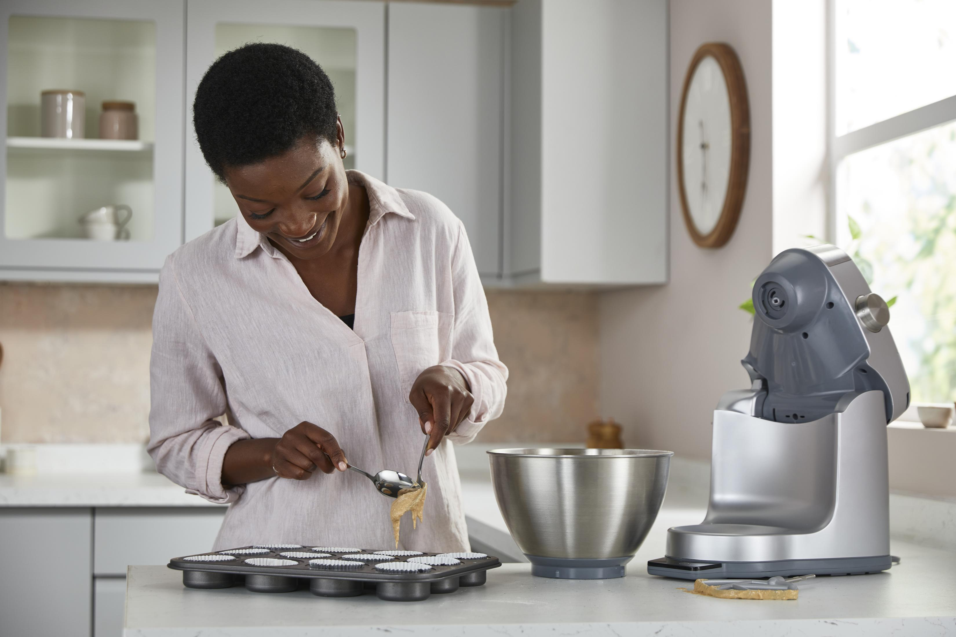 Una donna versa pastella in uno stampo per muffin. Un robot da cucina è vicino.