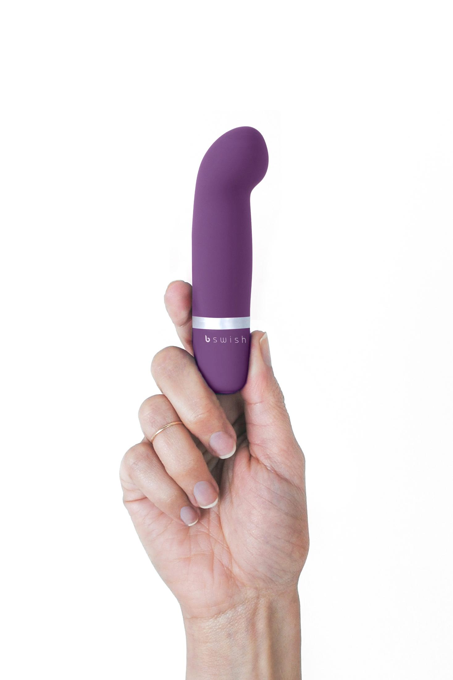 Eine Hand hält einen lila Vibrator mit silbernem Ring und dem Logo "b swish".
