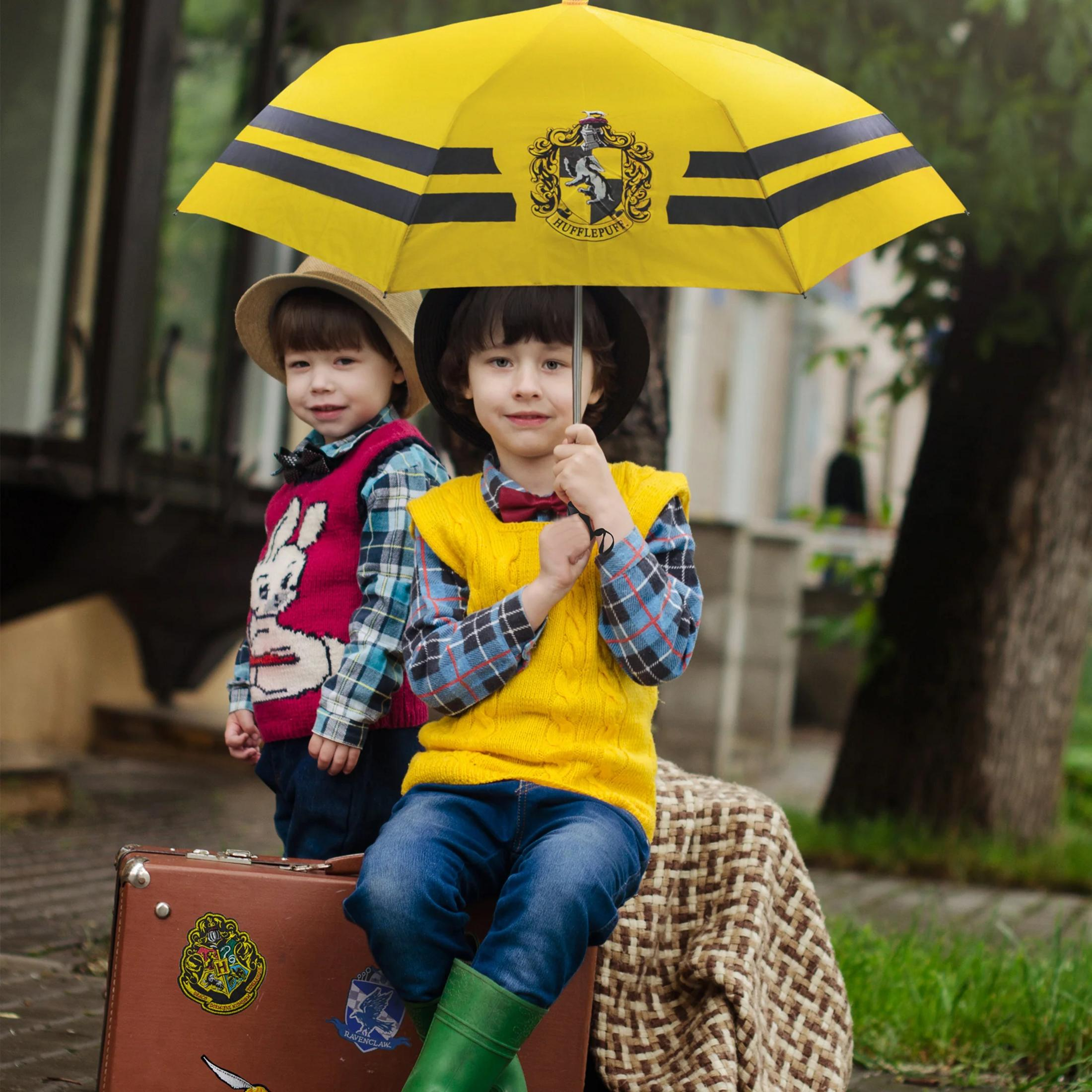 Dos niños bajo un paraguas amarillo de Harry Potter se sientan en una maleta.
