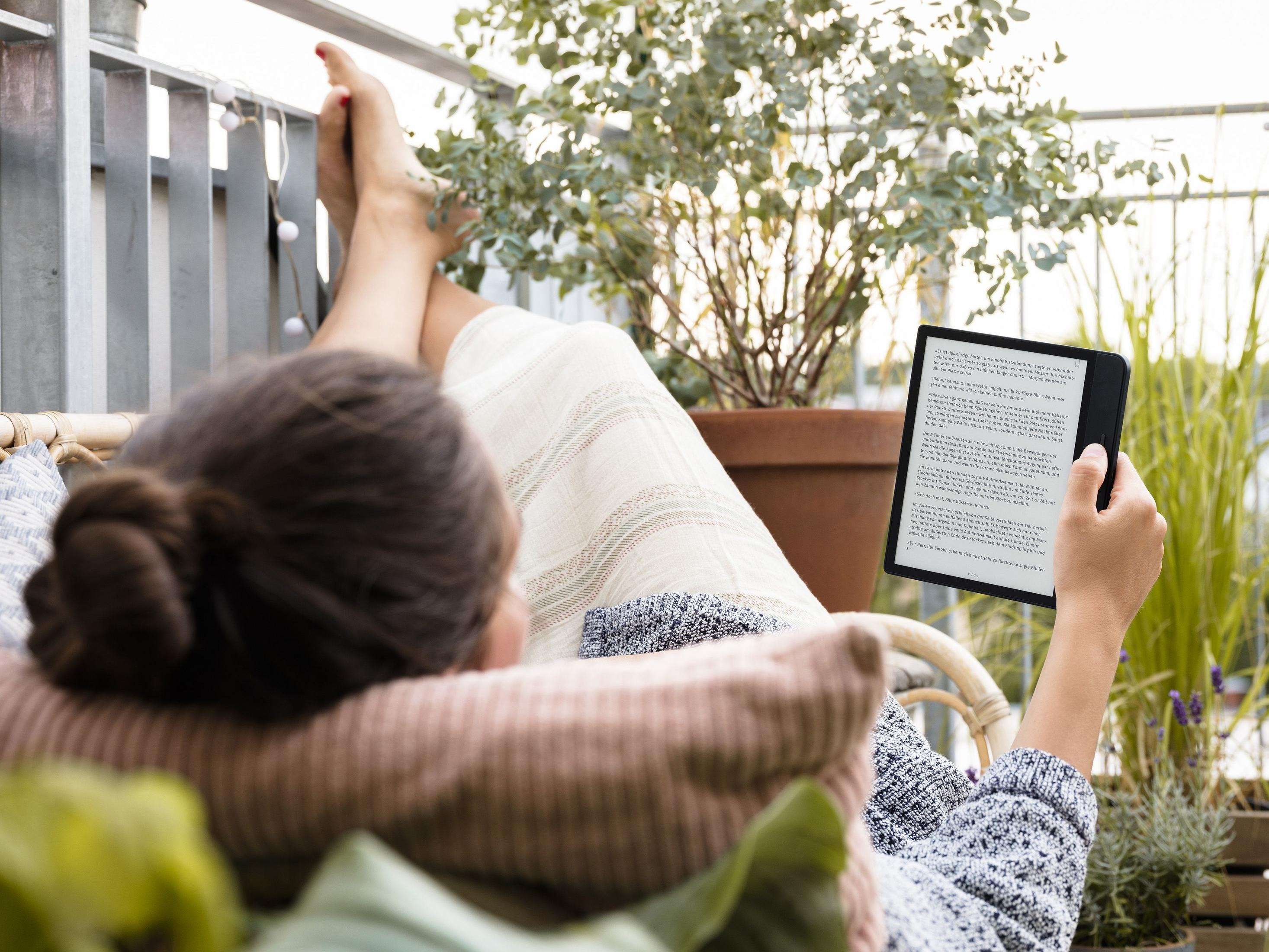 Eine Frau liest auf einem Balkon mit Pflanzen ein E-Book.