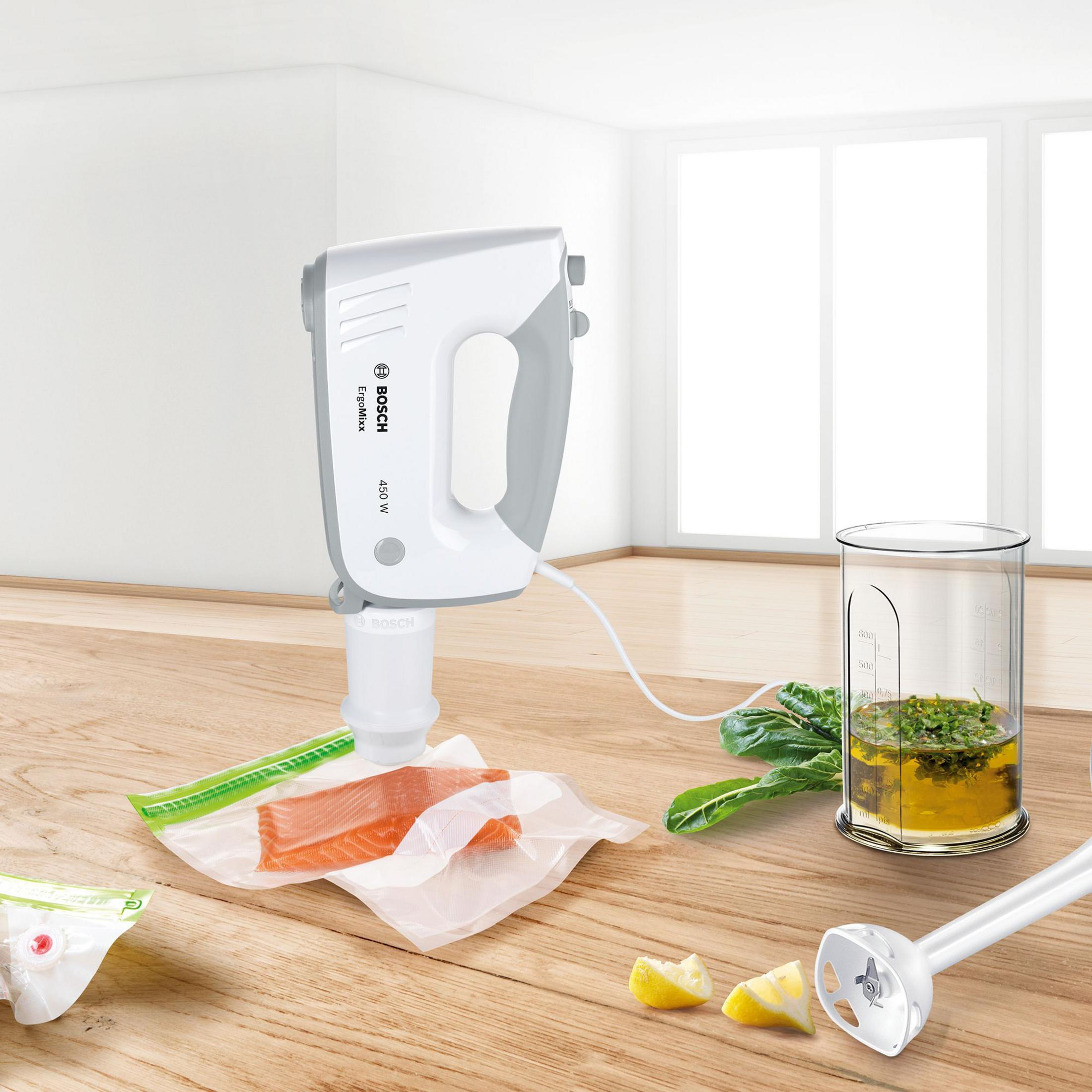 White hand mixer with cord, vacuum-sealed salmon, lemon, and herbs on a wooden table.