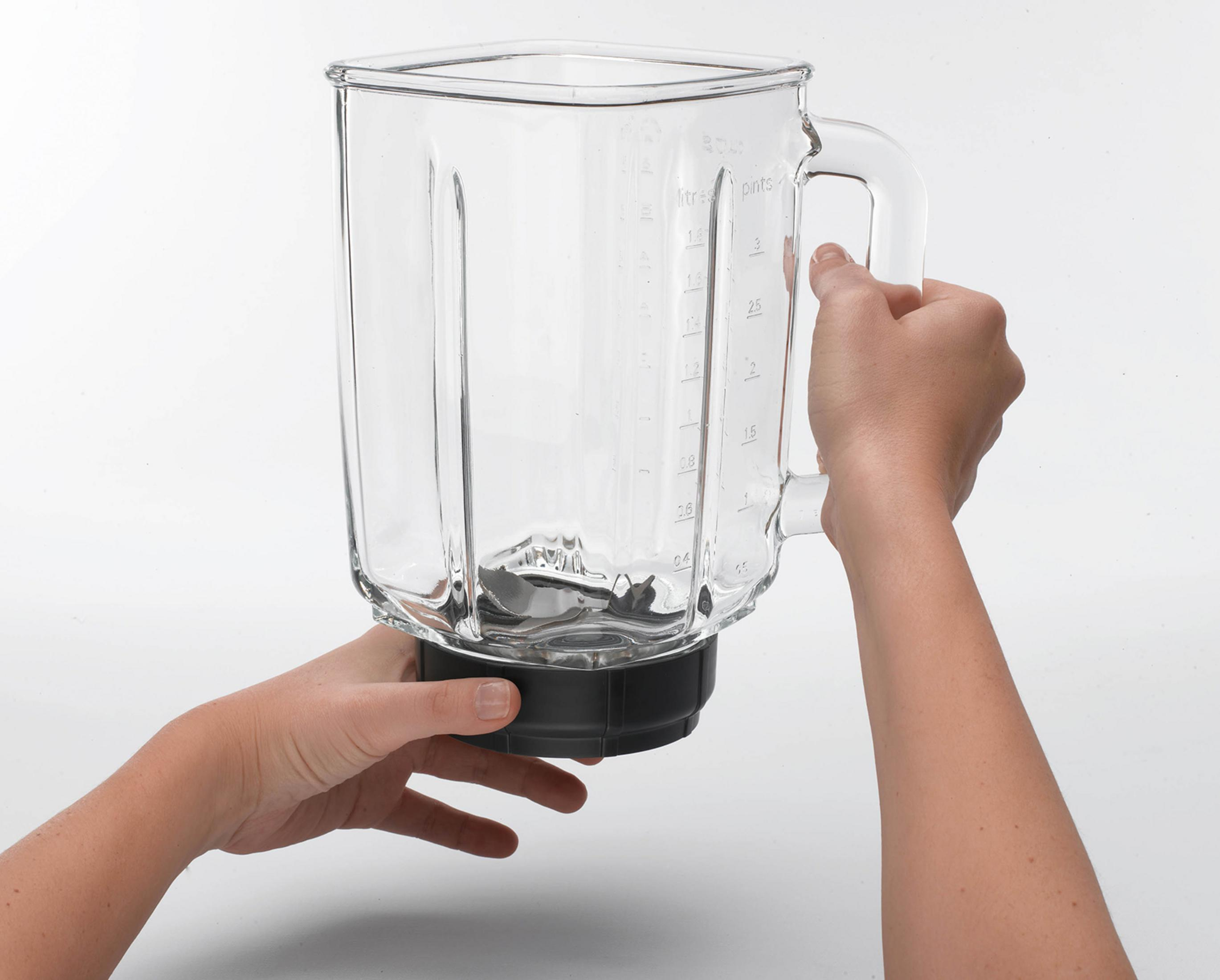 Ręce trzymają pusty szklany dzbanek blendera z oznaczeniami miar.